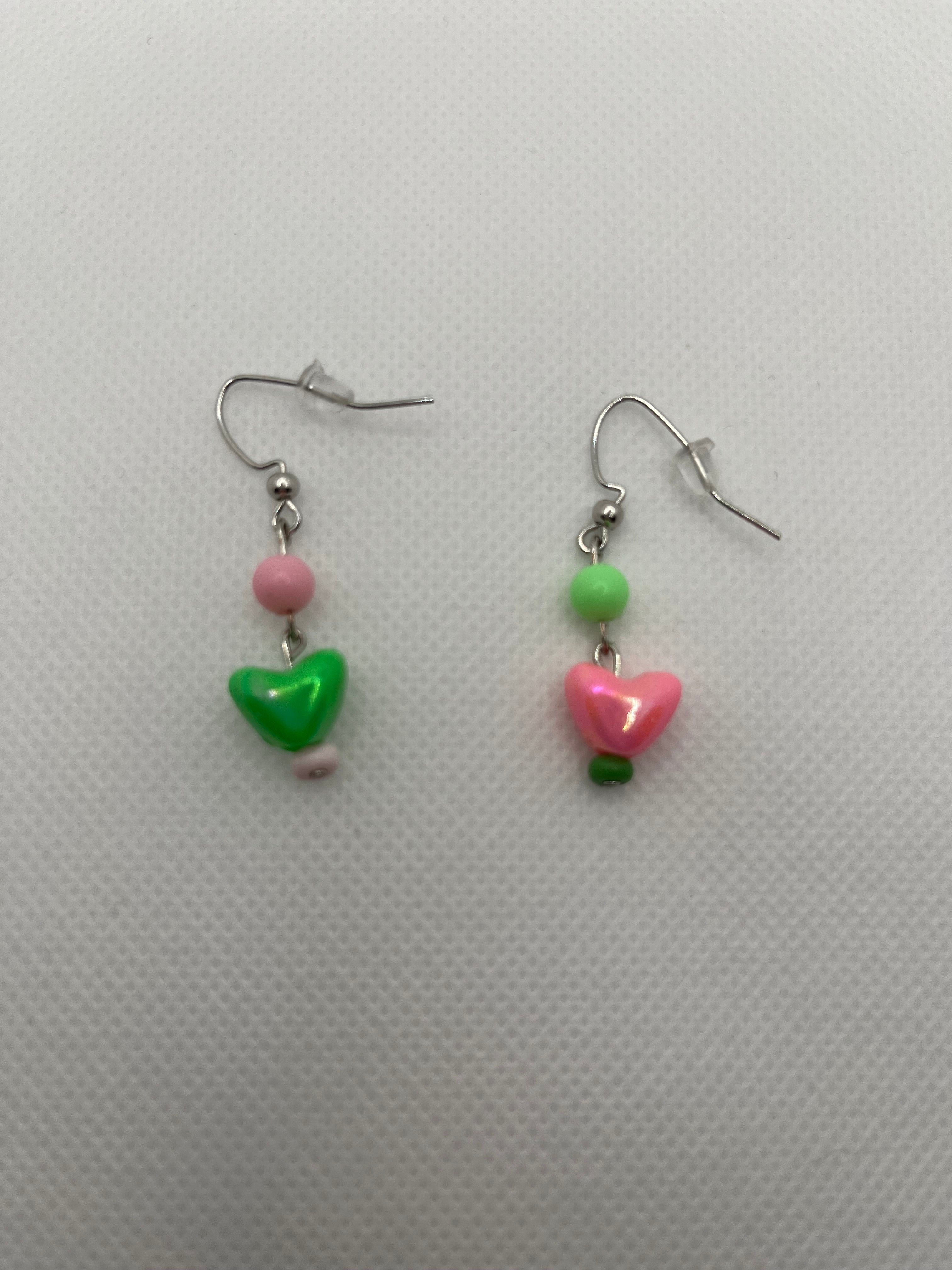 Pink and green alternate earrings with hearts on the end against a white background