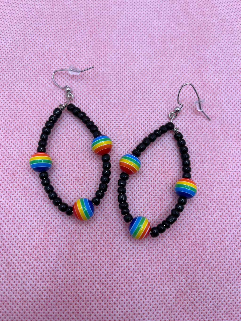 Black seed beads with rainbow beads throughout on earrings against a pink background