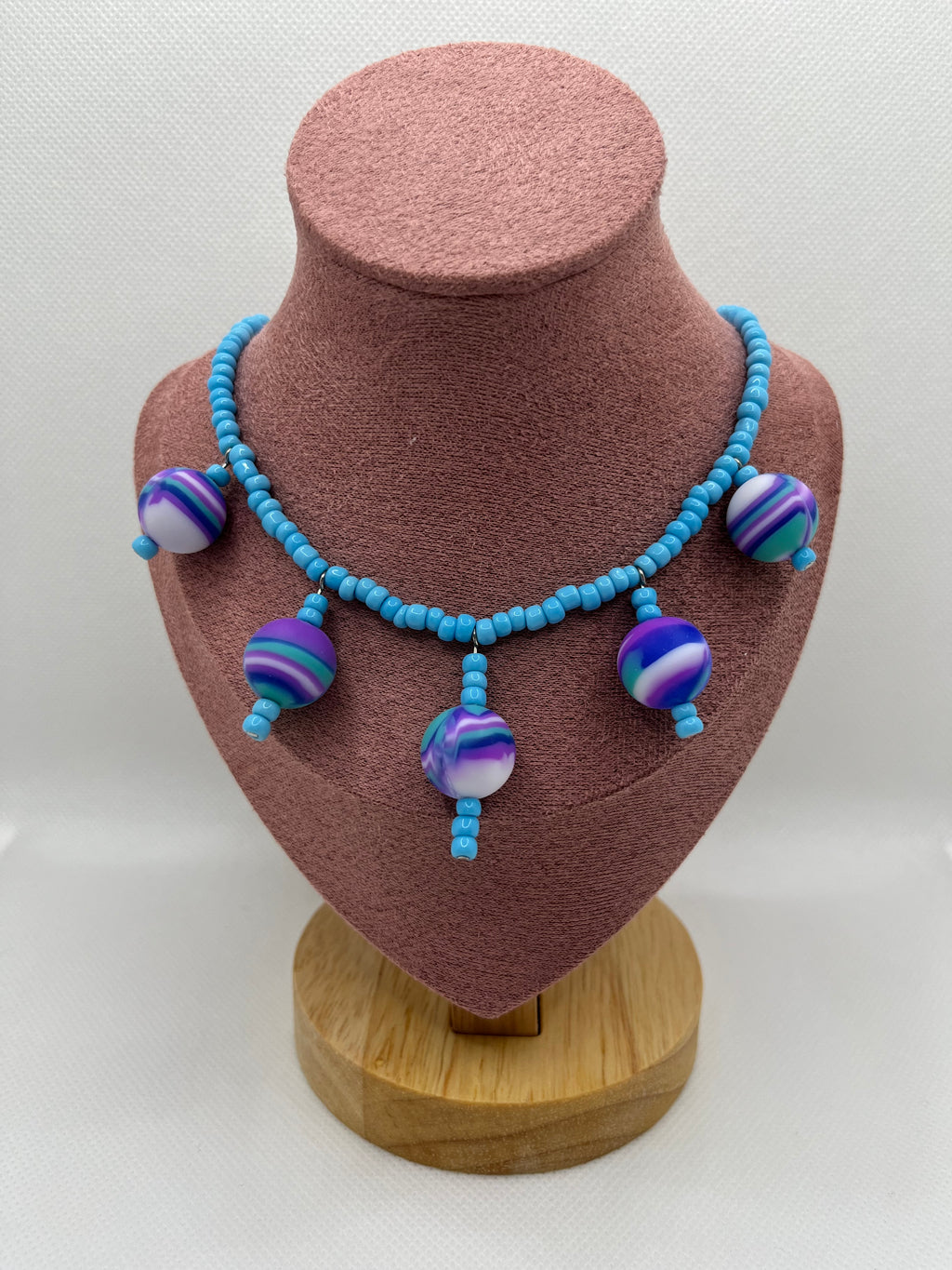 Blue seed bead necklace with silicone beads strung throughout draped over a blush pink mannequin with a white background.