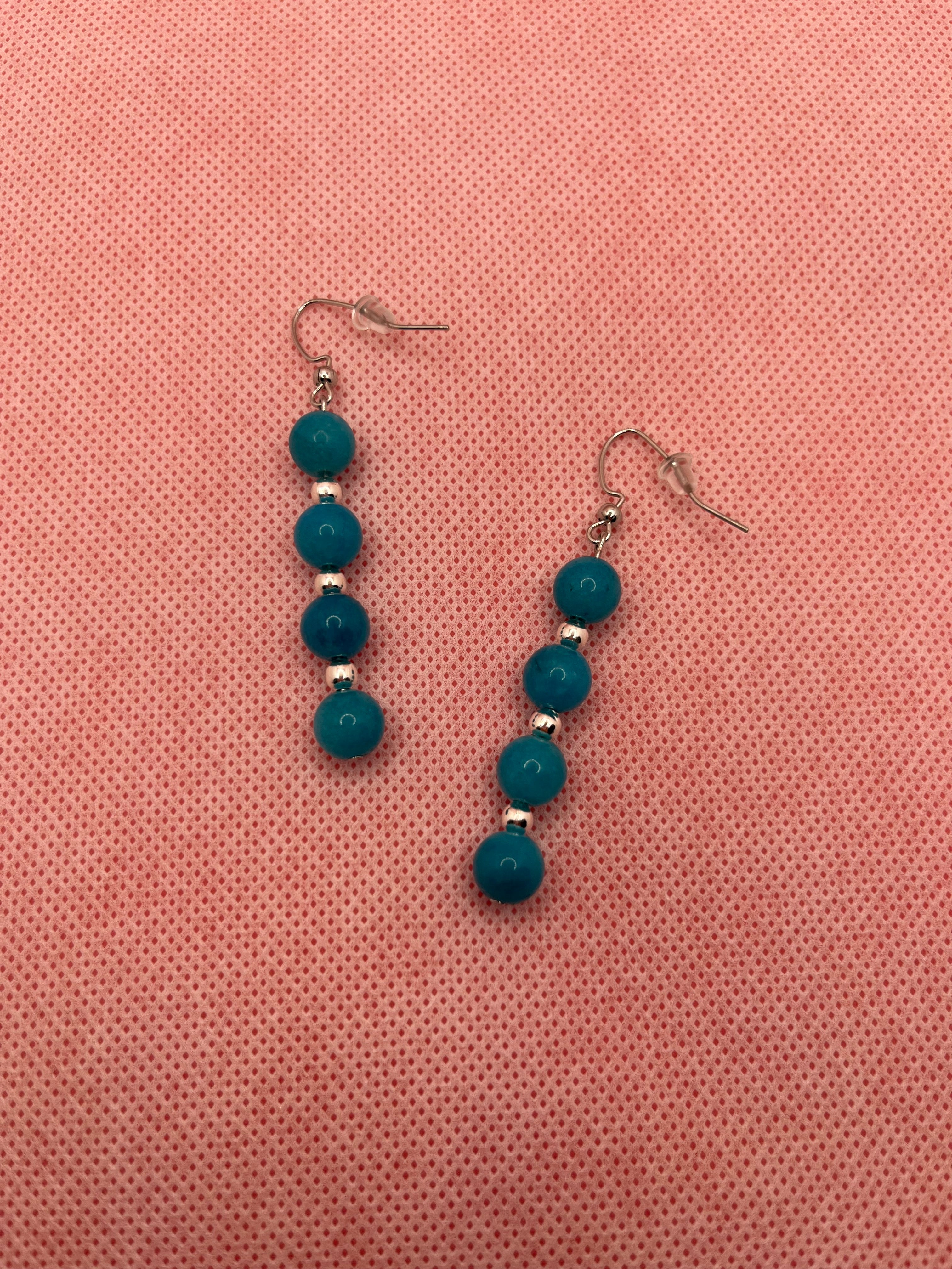 Four blue beads with silver spacer beads on silver earrings against a pink background