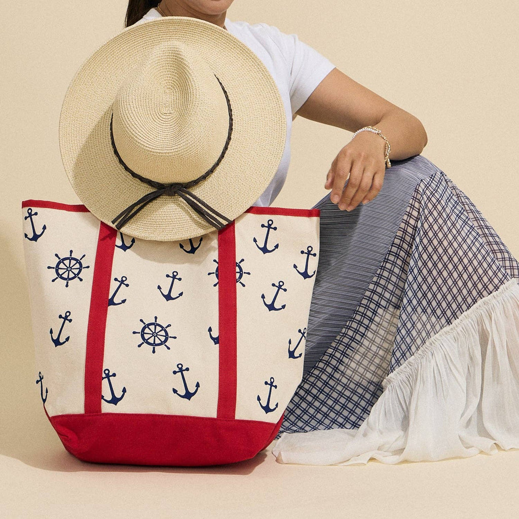 Person sitting with a tote bag featuring nautical patterns and a straw hat.