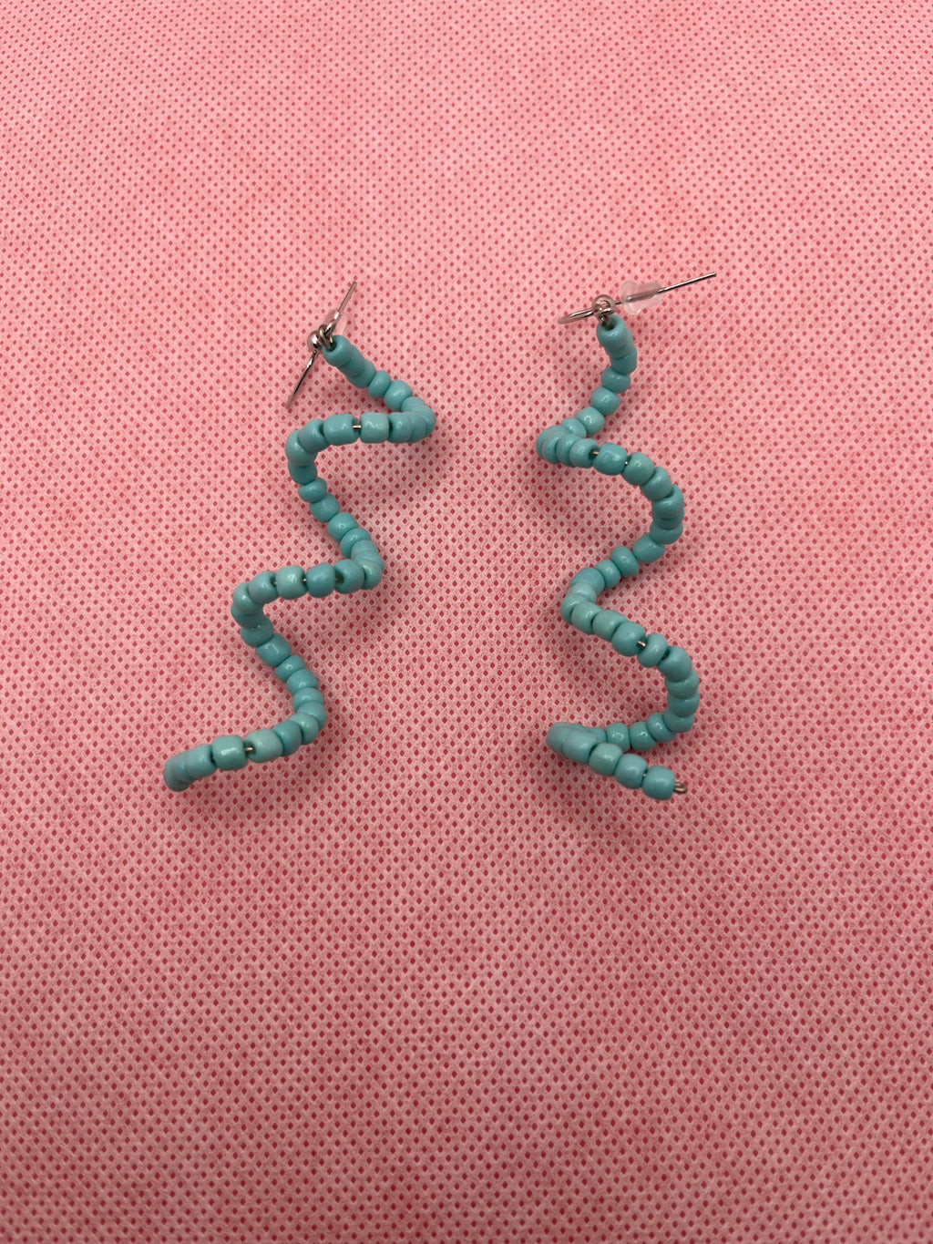Light blue seed bead spiral earrings against a pink background