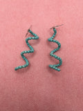 Light blue seed bead spiral earrings against a pink background