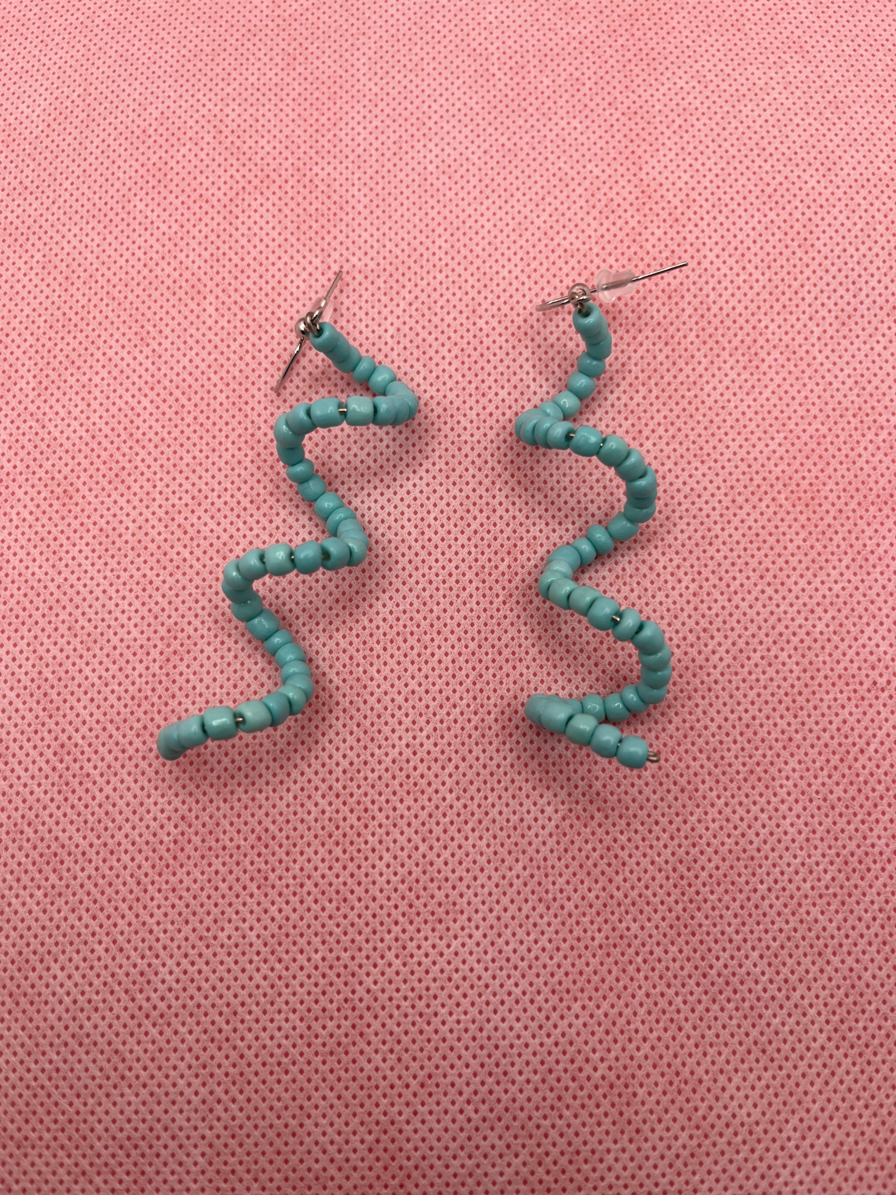Light blue seed bead spiral earrings against a pink background
