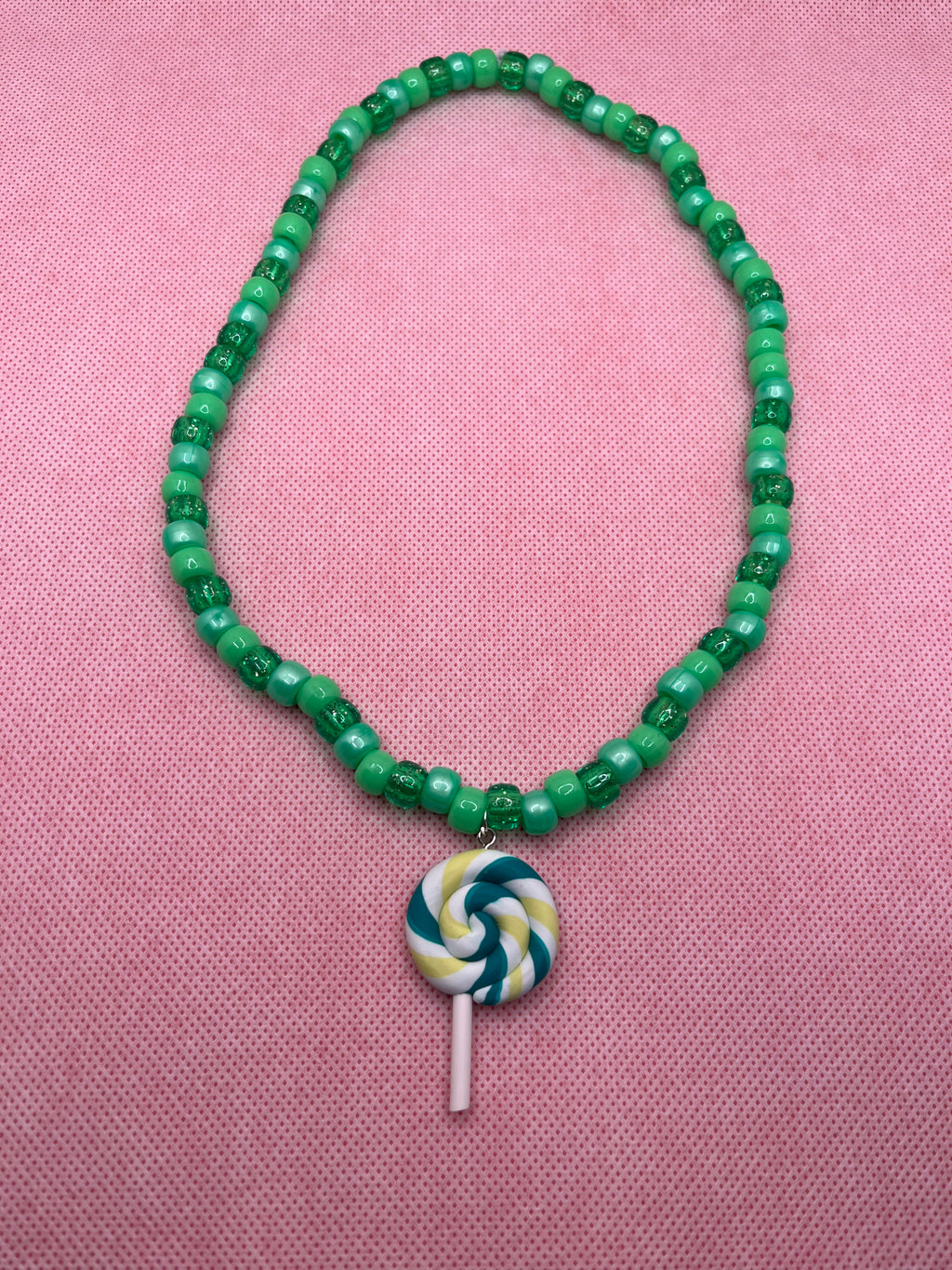Green beaded necklace with green lollipop pendant on a pink background