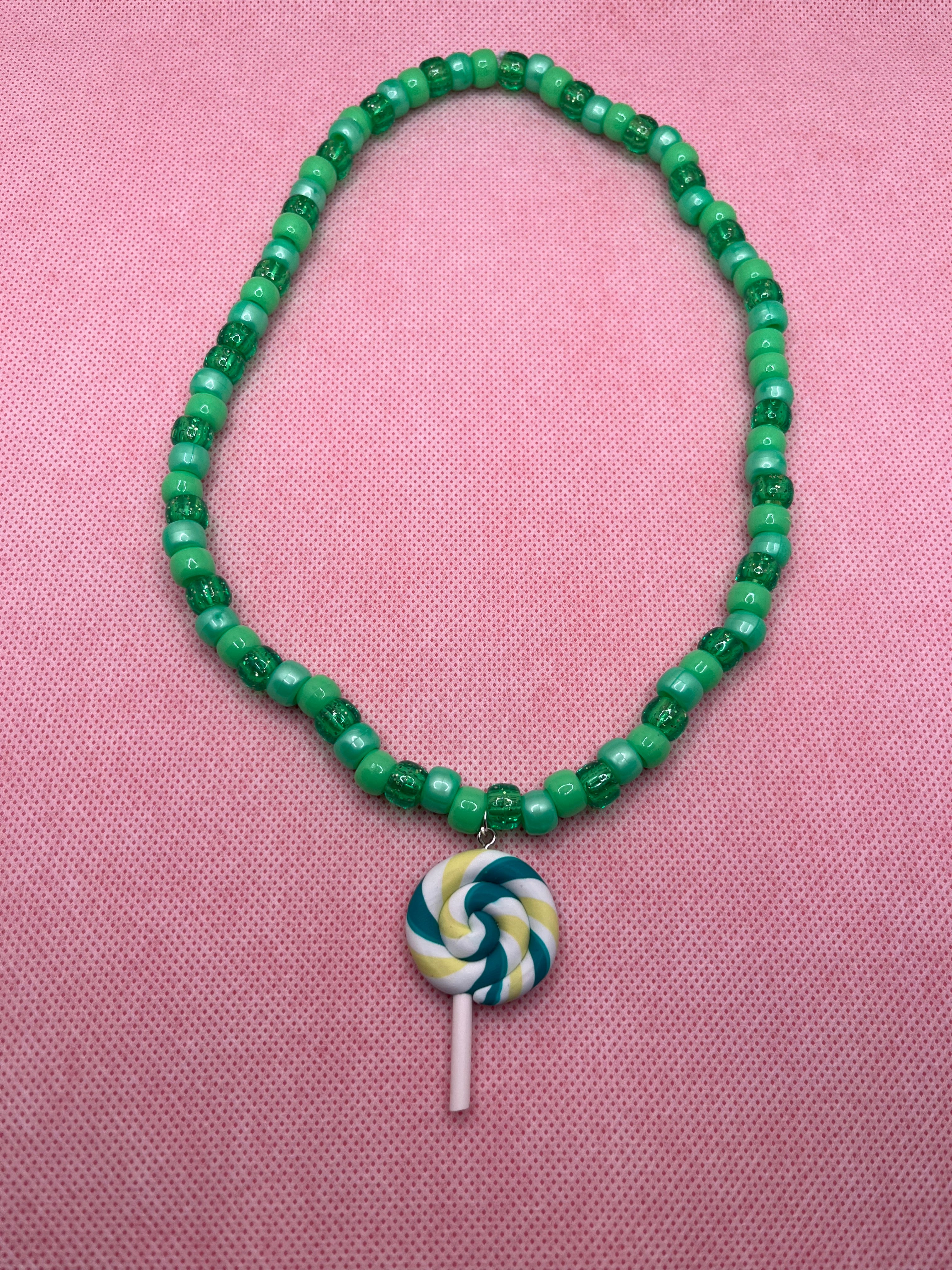 Green beaded necklace with green lollipop pendant on a pink background