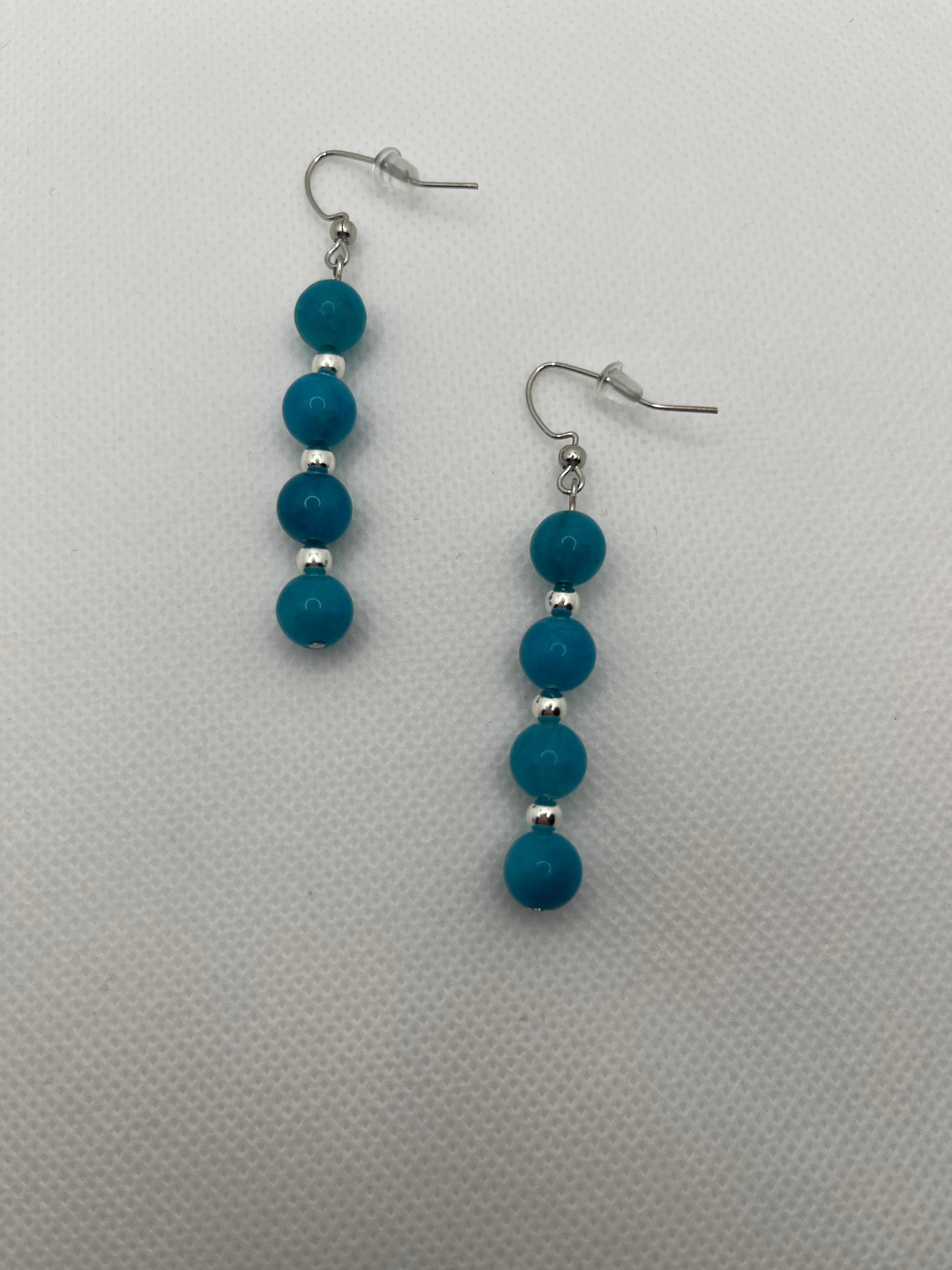 Four blue beads with silver spacer beads on silver earrings against a white background