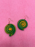 Green and yellow circle swirl earrings against a pink background