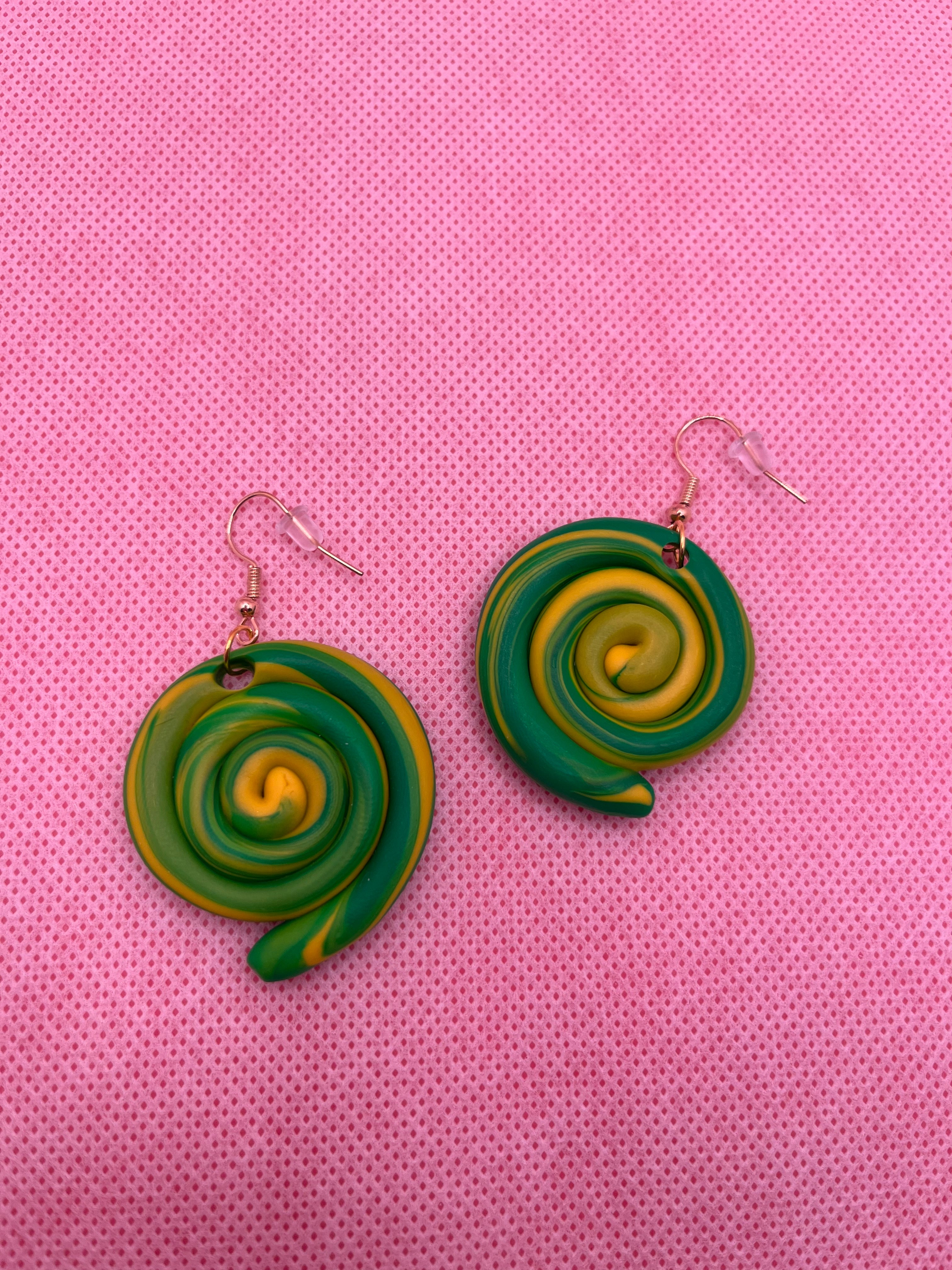 Green and yellow circle swirl earrings against a pink background