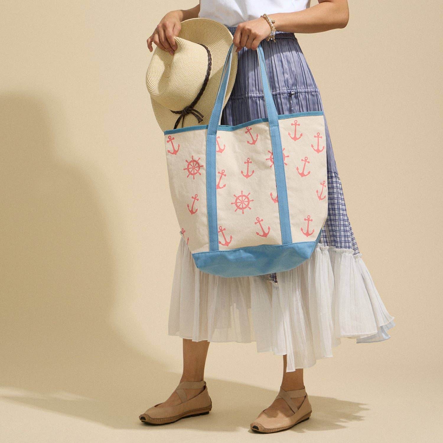 Person holding a tote bag with anchor pattern against a beige background