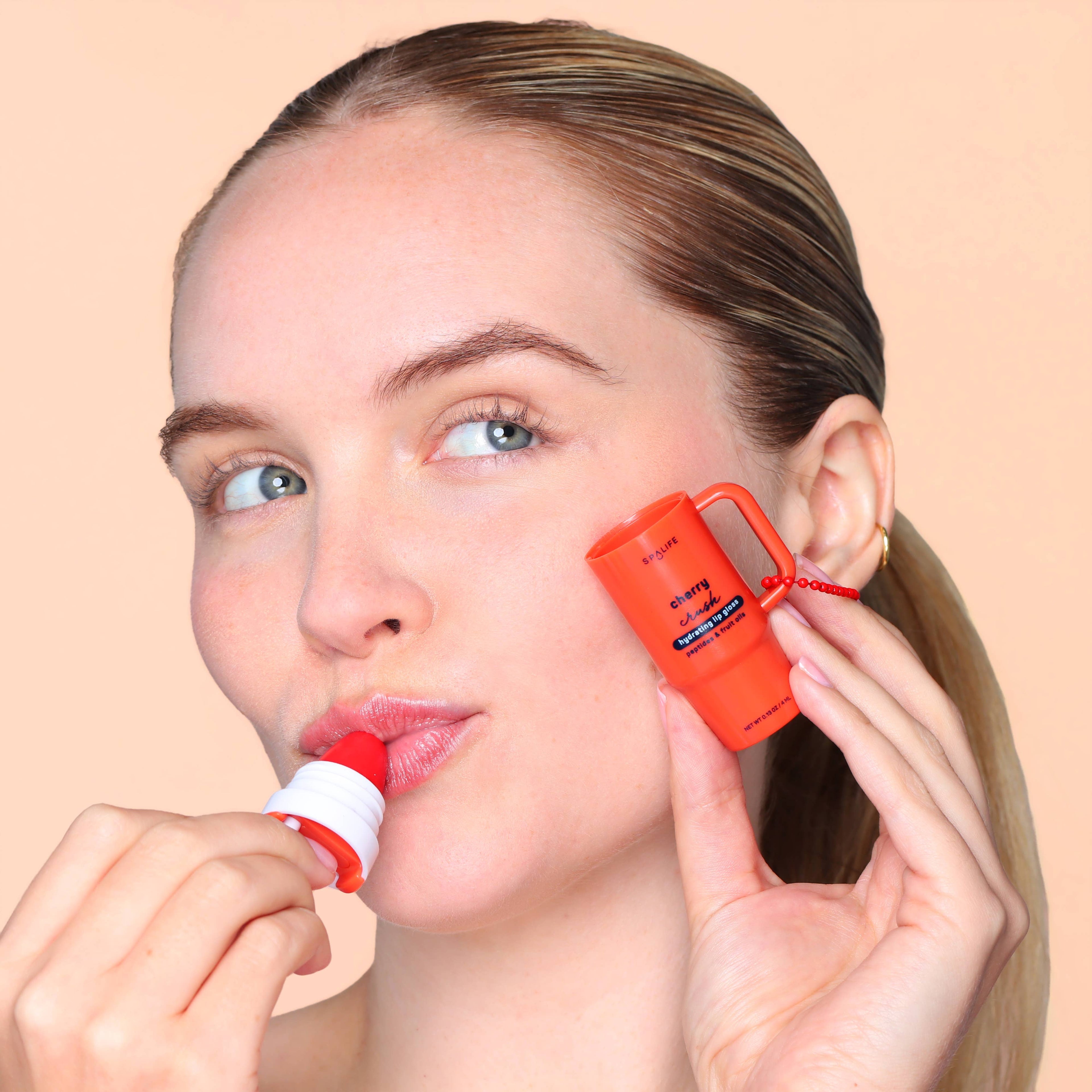 Woman applying a red lip balm to her lips with a matching red case on a beige background