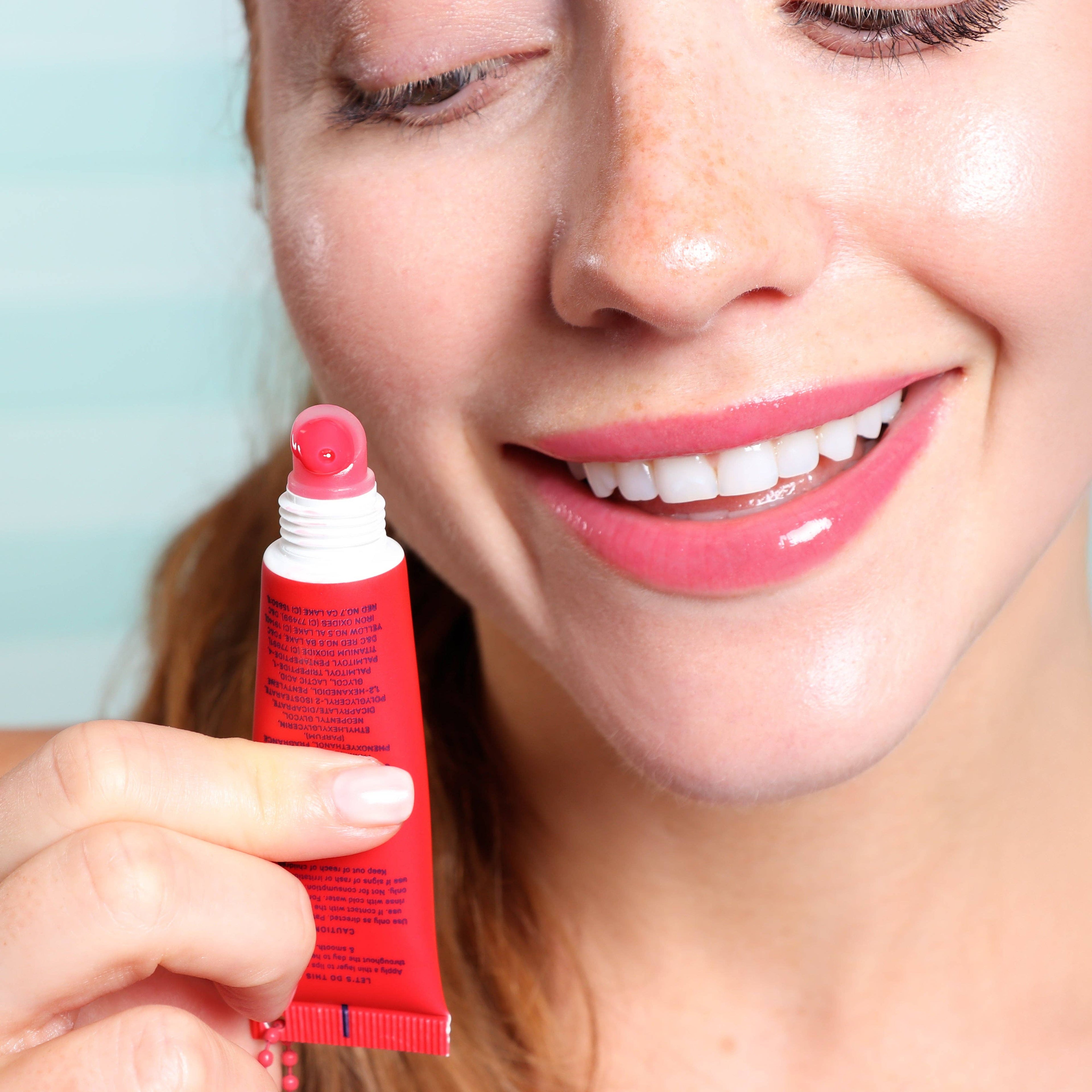 Woman holding a red lip balm tube with a light blue background
