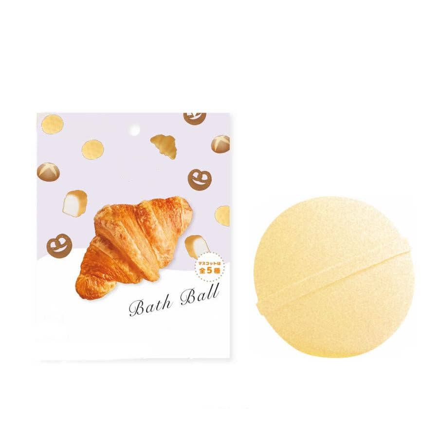 Yellow bath bomb with a decorative card featuring a croissant design on a white background