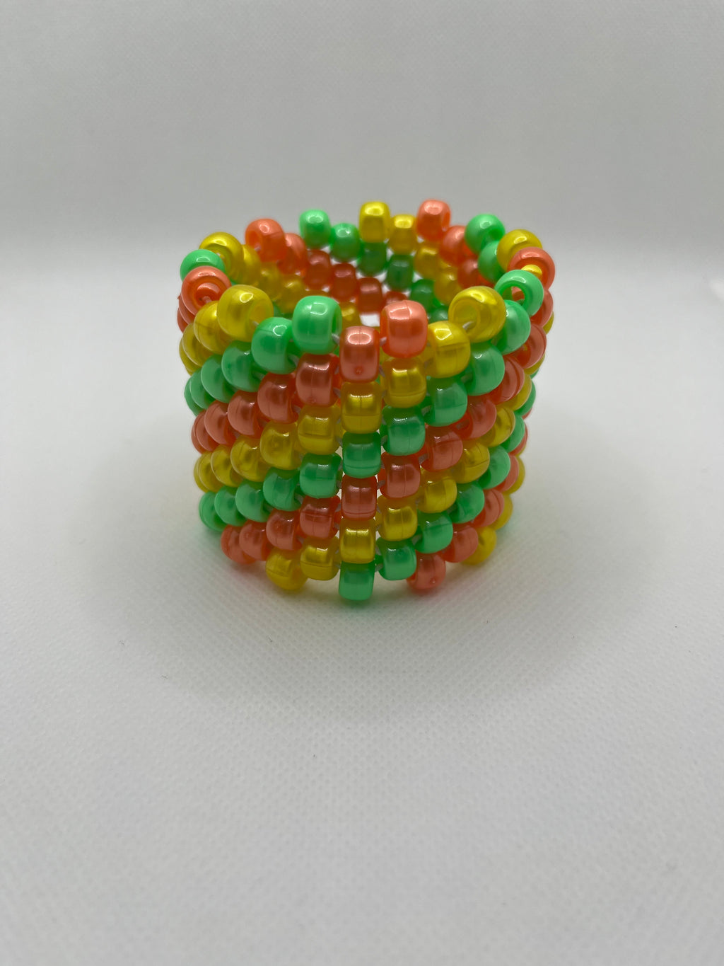 Orange, yellow, and green spiral beaded cuff bracelet against a white background