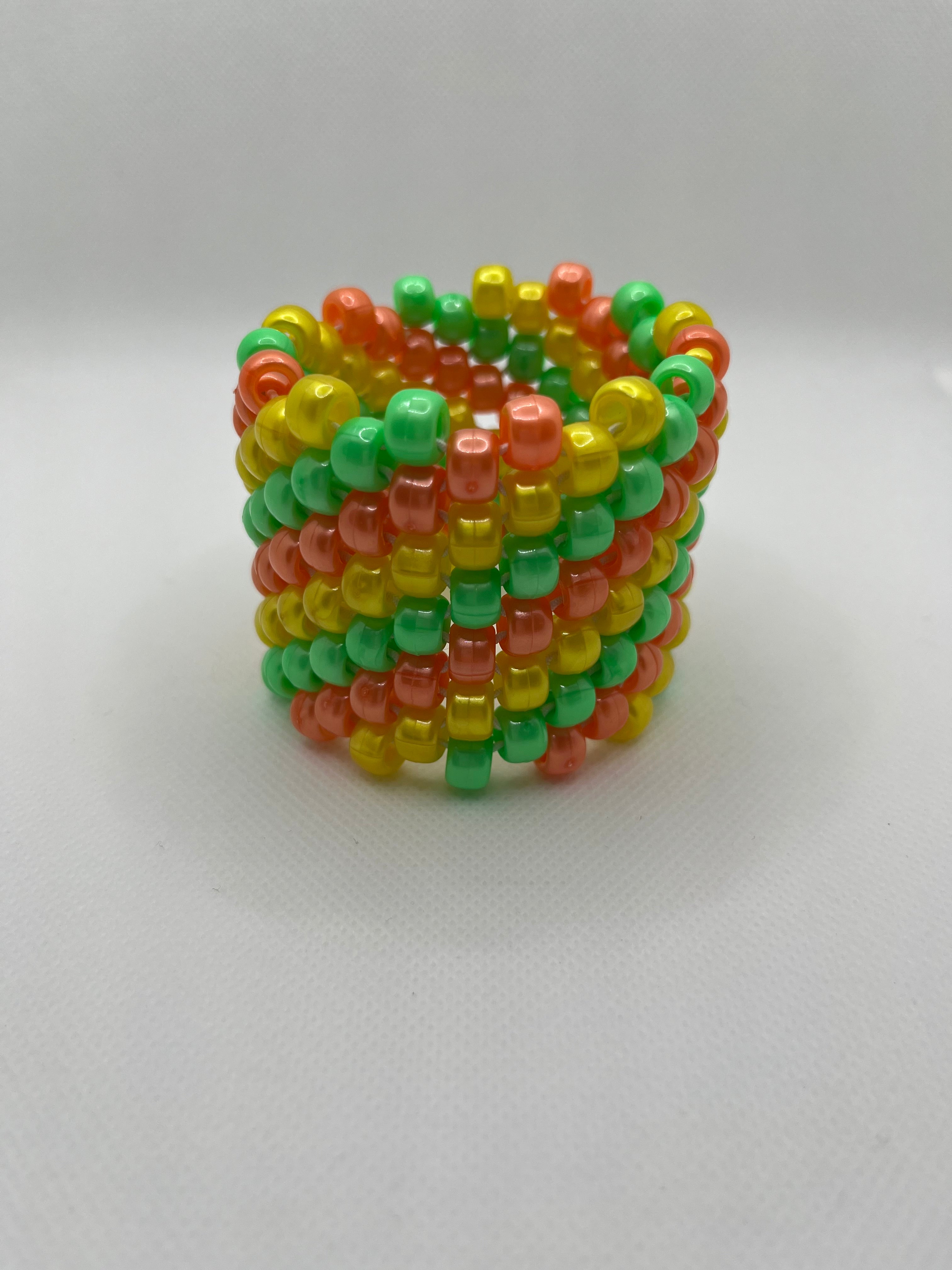 Orange, yellow, and green spiral beaded cuff bracelet against a white background