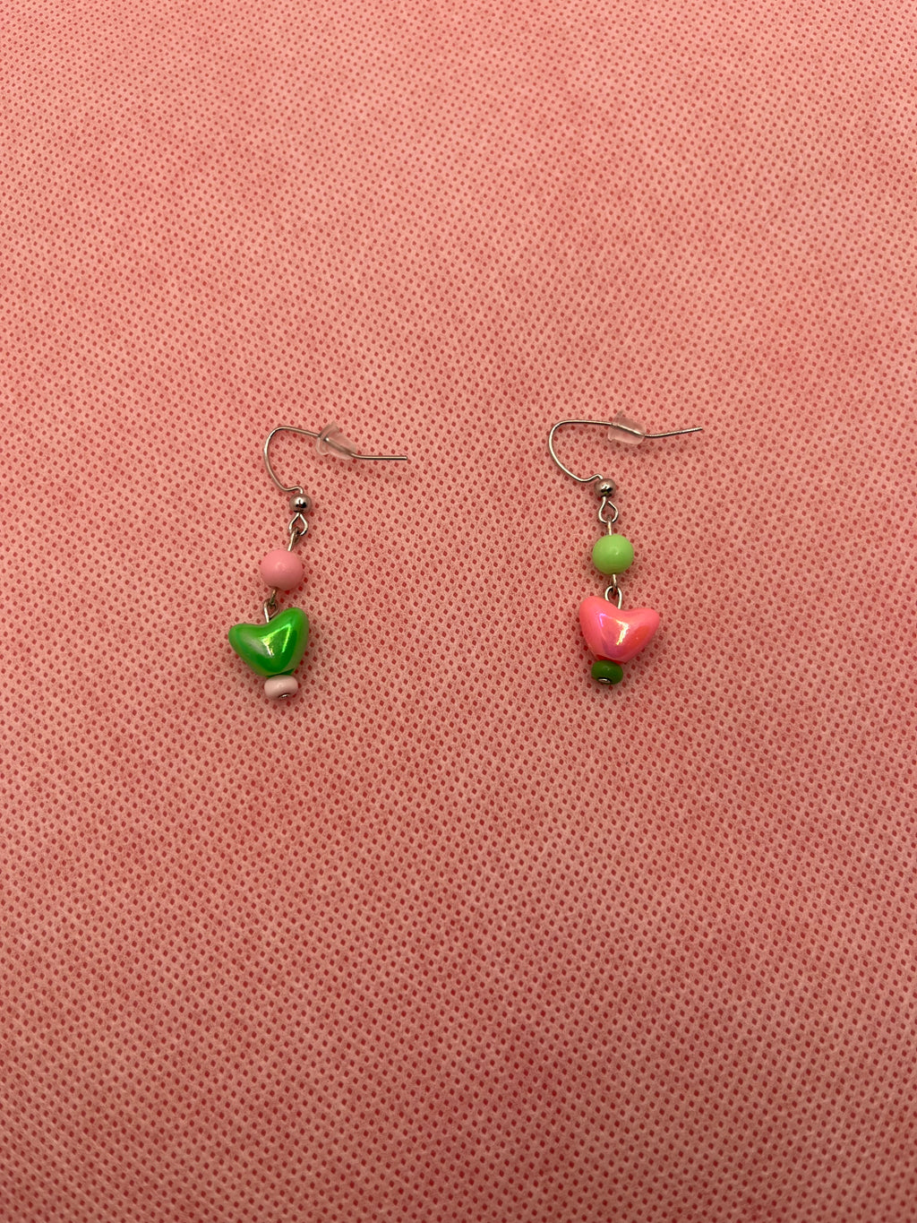 Pink and green alternate earrings with hearts on the end against a pink background