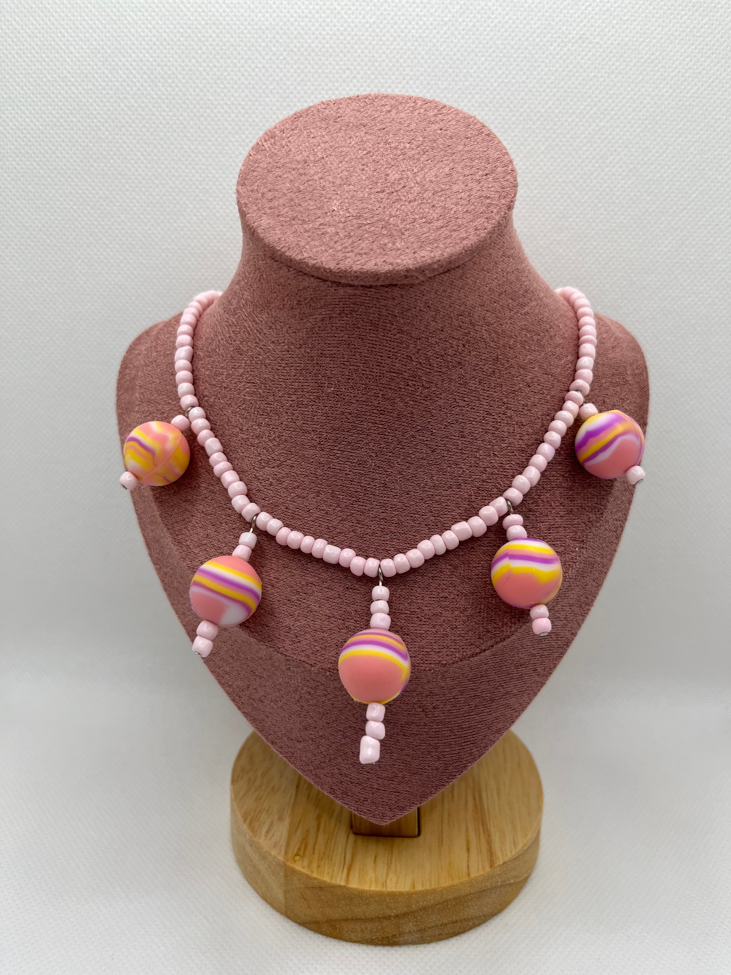 Pink seed bead necklace with silicone beads strung throughout draped over a blush pink mannequin with a white background.