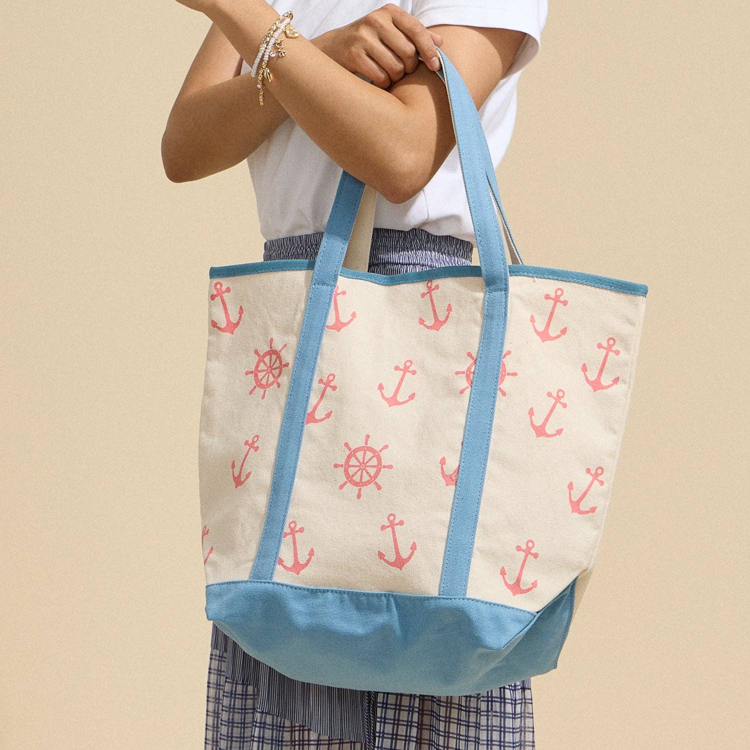 Person holding a tote bag with anchor and wheel pattern on a beige background