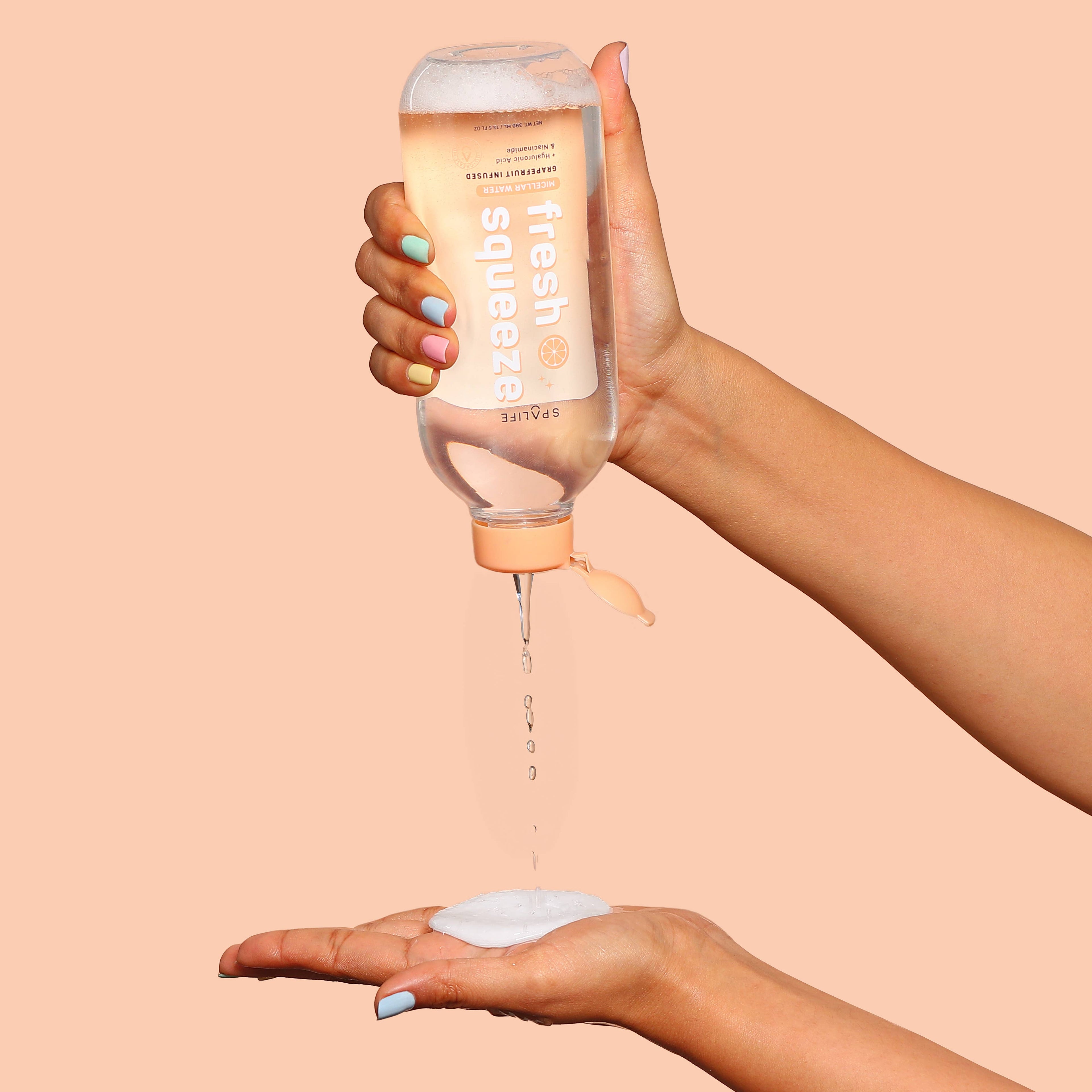 Hand holding a bottle of micellar water over another hand on a peach background