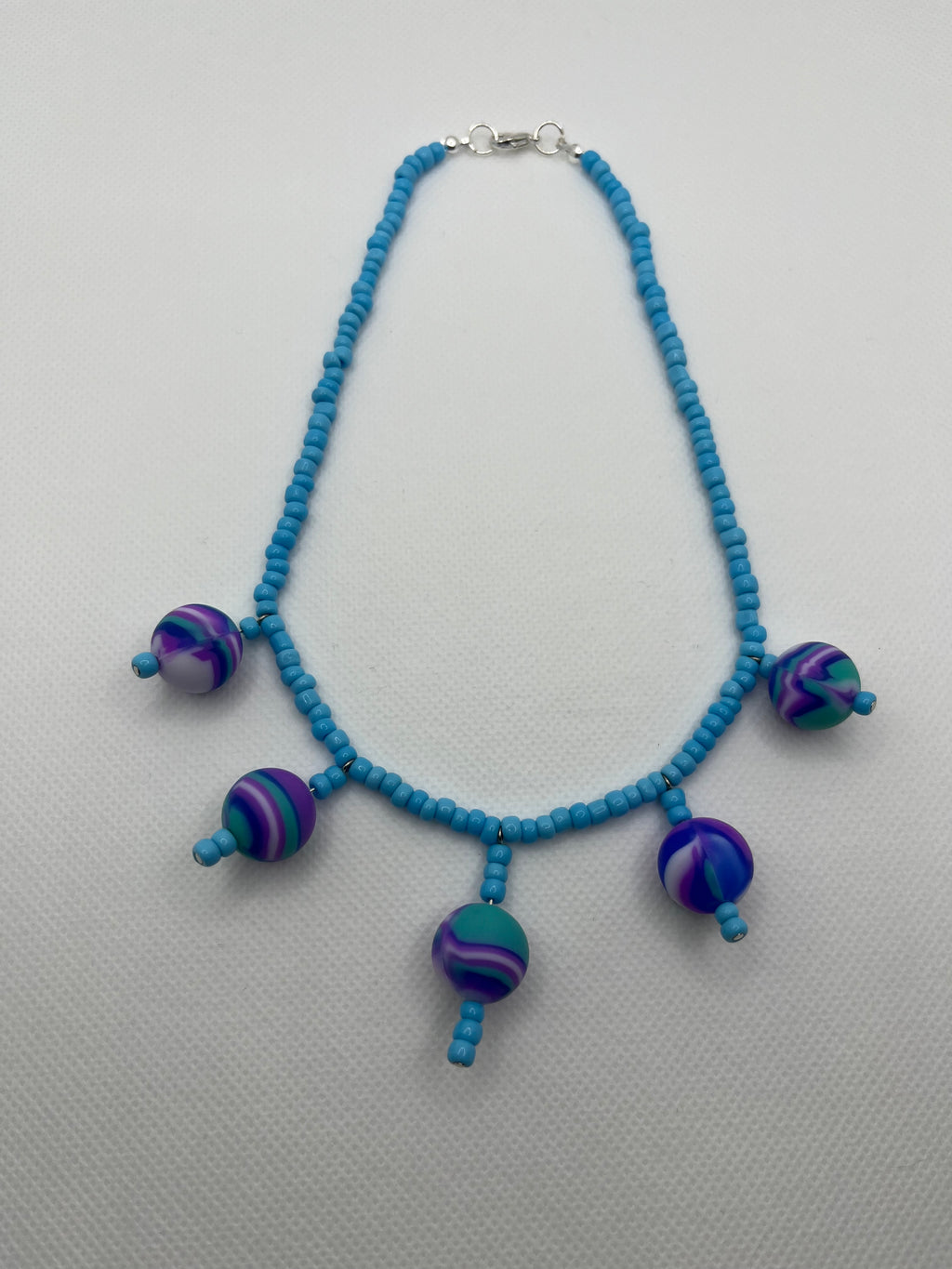 Blue seed bead necklace with silicone beads strung throughout laid flat against a white background.