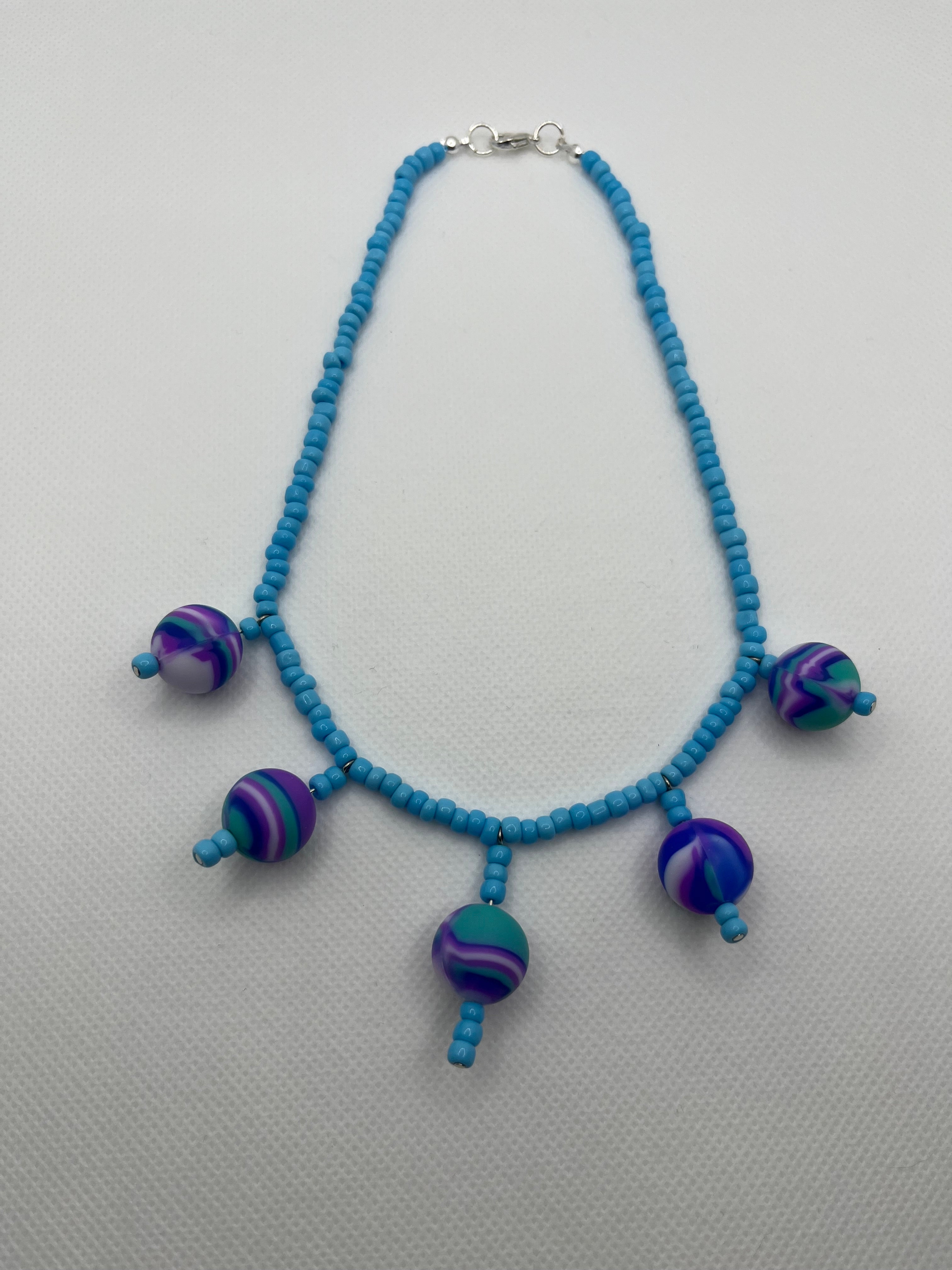 Blue seed bead necklace with silicone beads strung throughout laid flat against a white background.