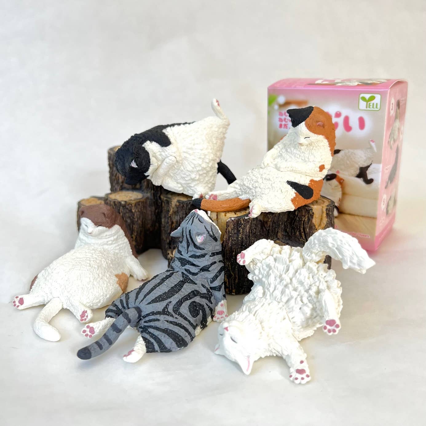 Cat-shaped toys on wooden logs with a pink box in the background