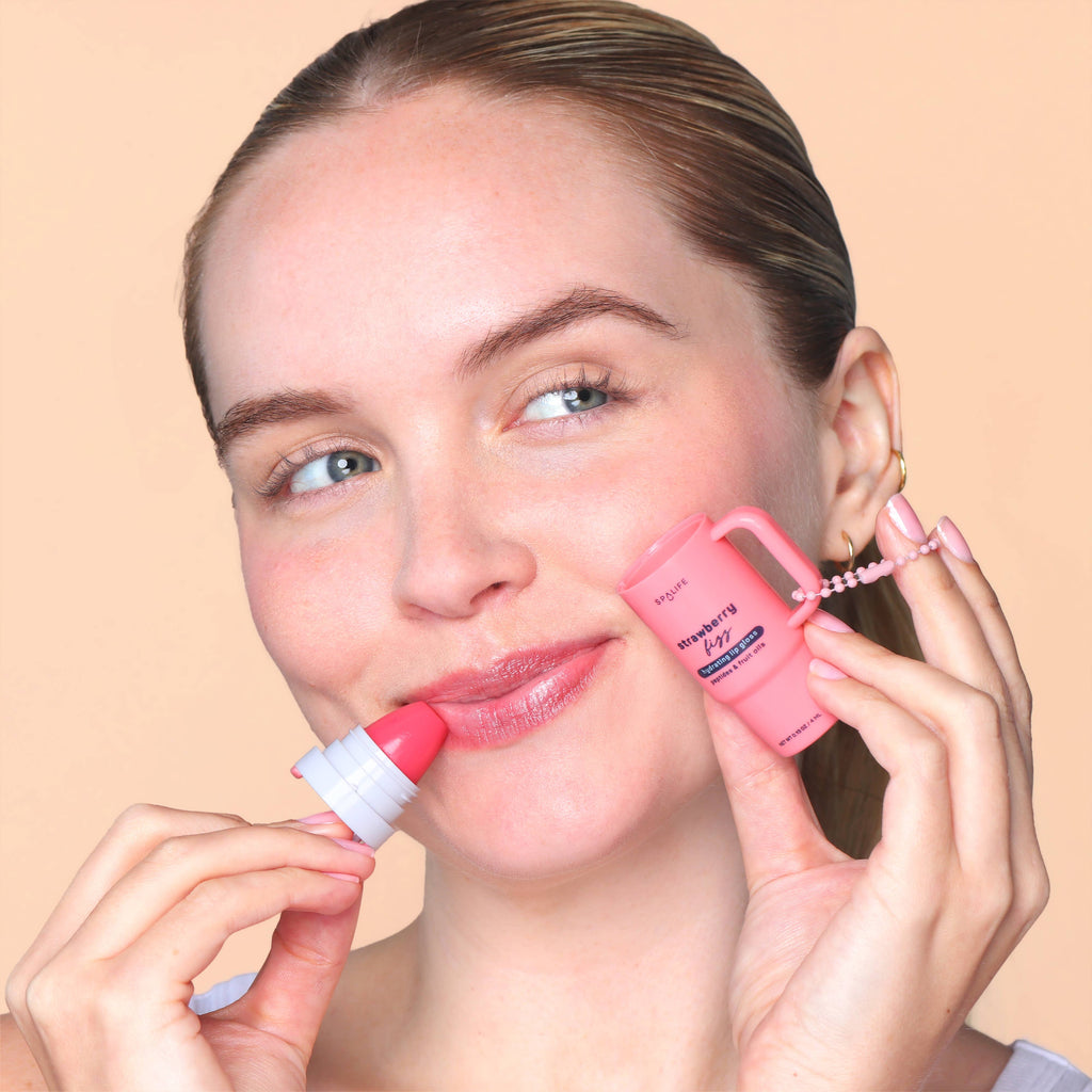 Woman applying pink lip balm to her lips with a beige background