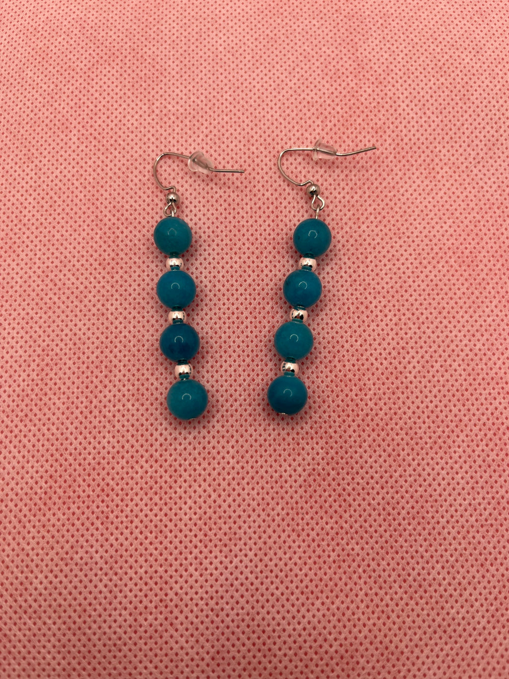 Four blue beads with silver spacer beads on silver earrings against a pink background