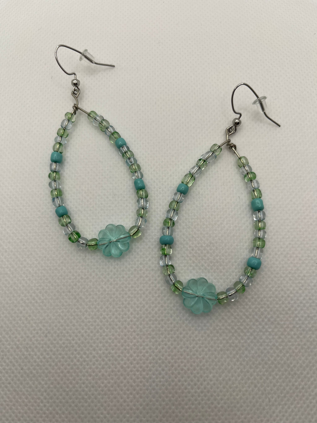 Blue and green beaded earrings with a large transparent clover bead on the bottom against a white background
