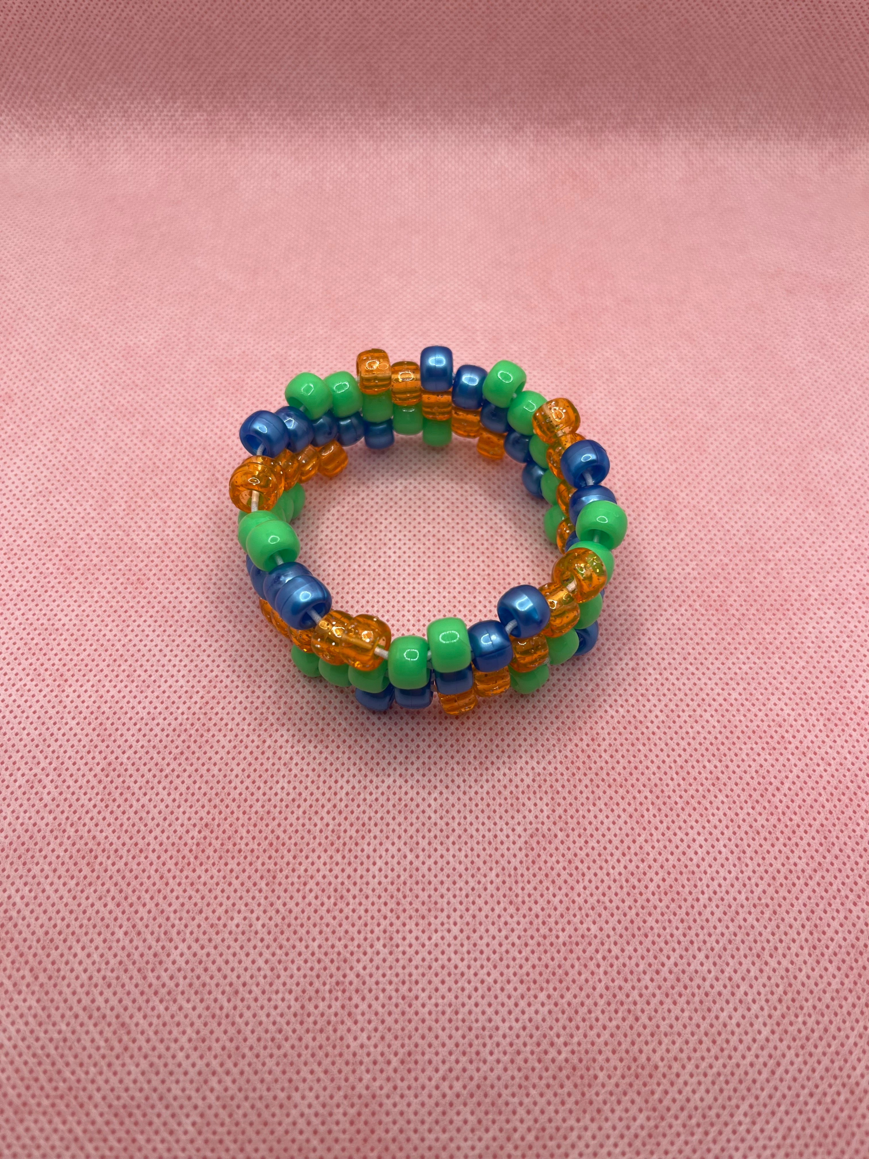 Orange, blue, and green spiral small beaded cuff bracelet against a pink background