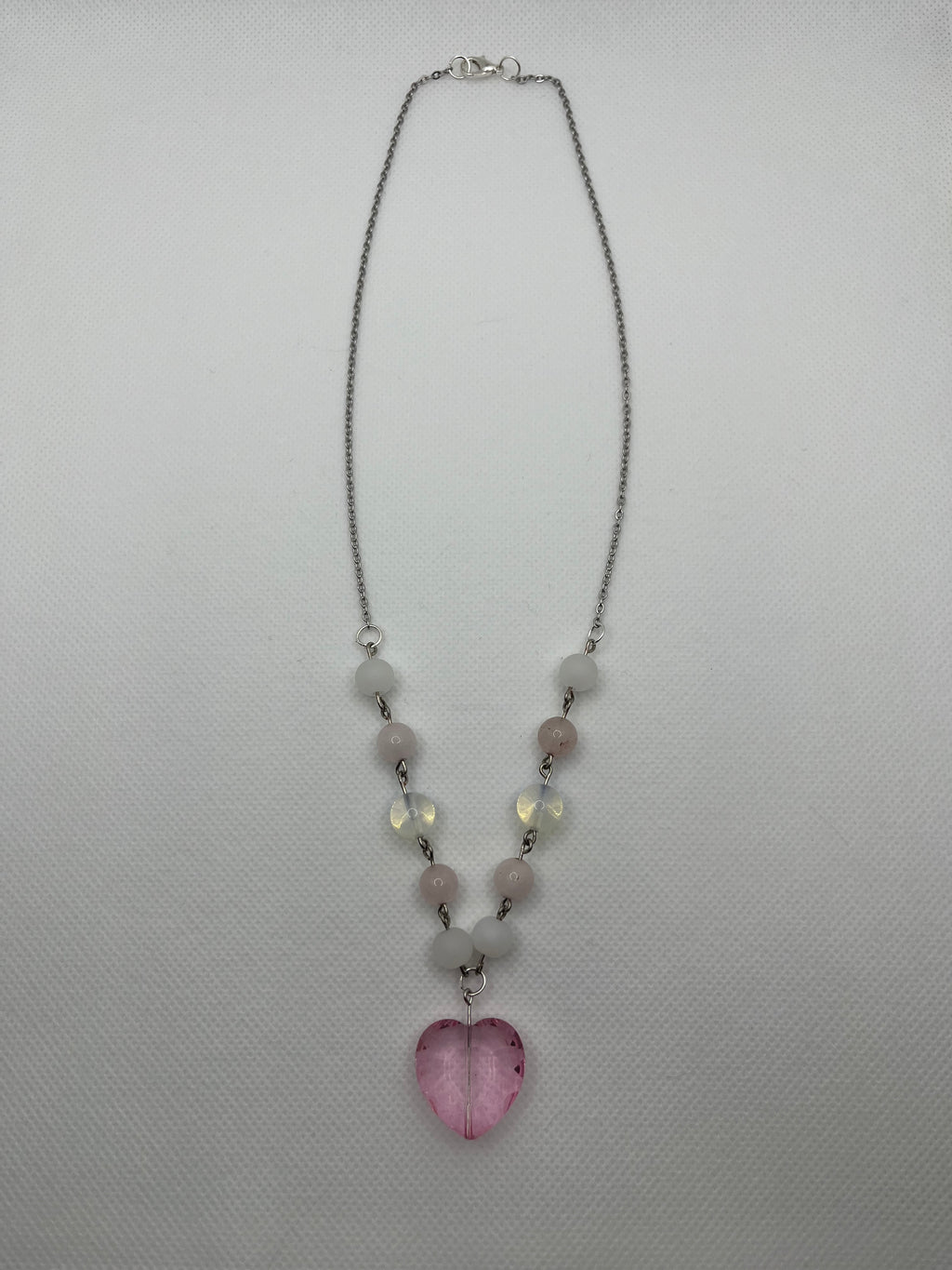 Pink and white necklace with a heart-shaped pendant laid flat on a white background.