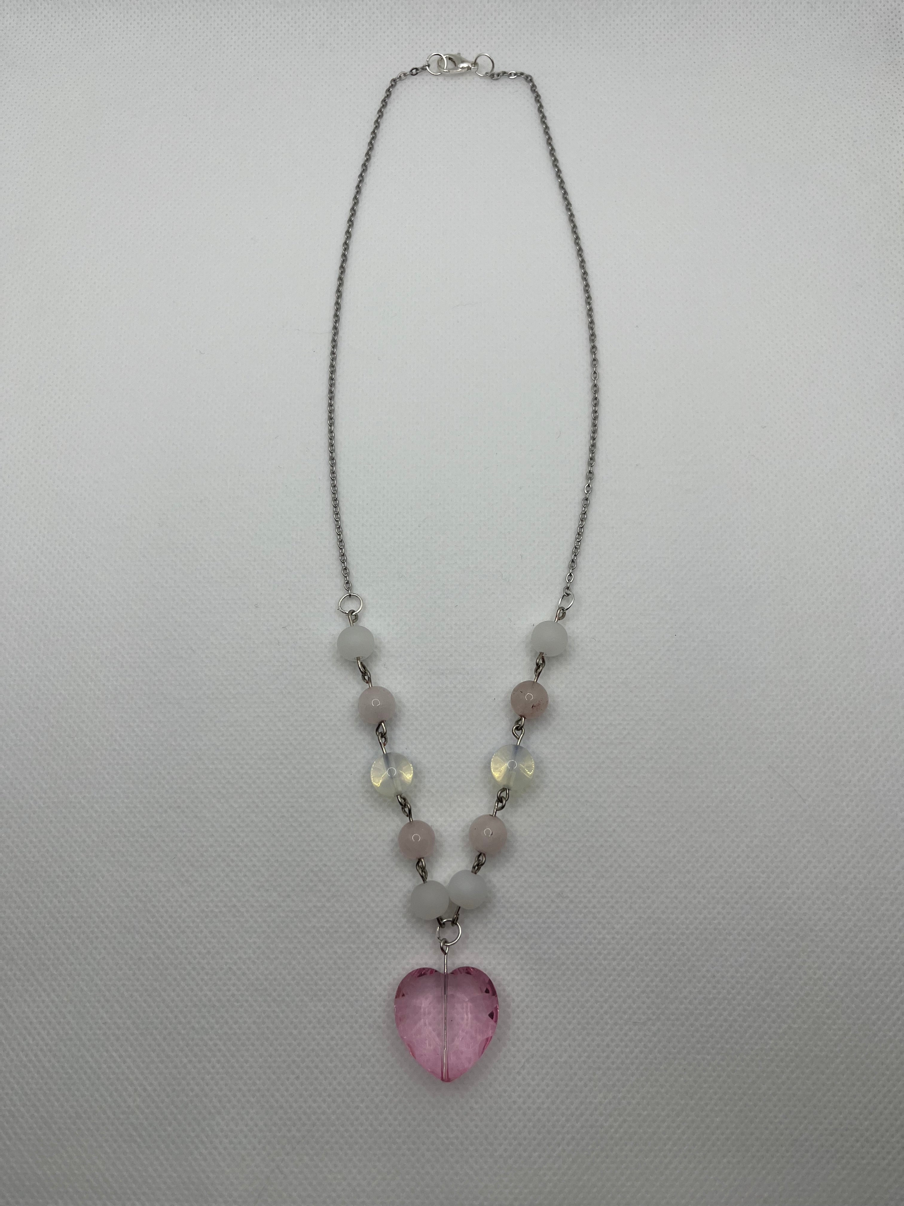 Pink and white necklace with a heart-shaped pendant laid flat on a white background.