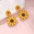 Sunflower-shaped earrings with yellow petals and brown centers on a light pink background