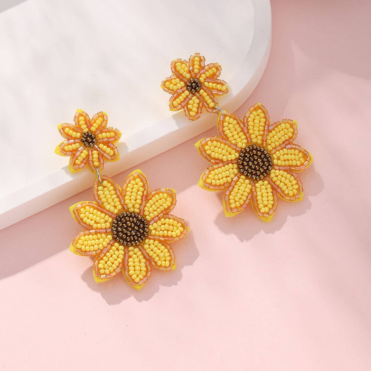 Sunflower-shaped earrings with yellow petals and brown centers on a light pink background