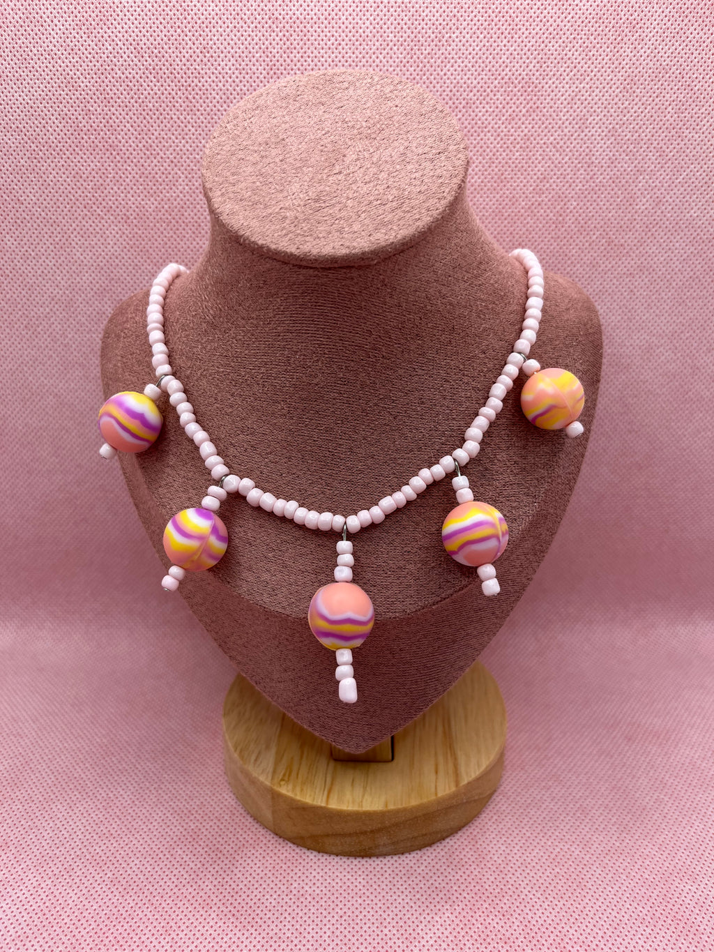 Pink seed bead necklace with silicone beads strung throughout draped over a blush pink mannequin with a pink background.