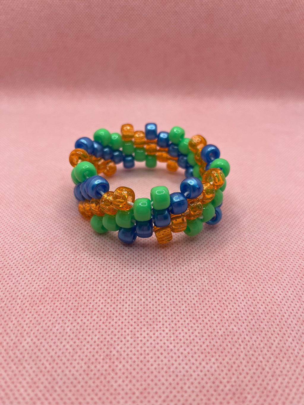 Orange, blue, and green spiral small beaded cuff bracelet against a pink background