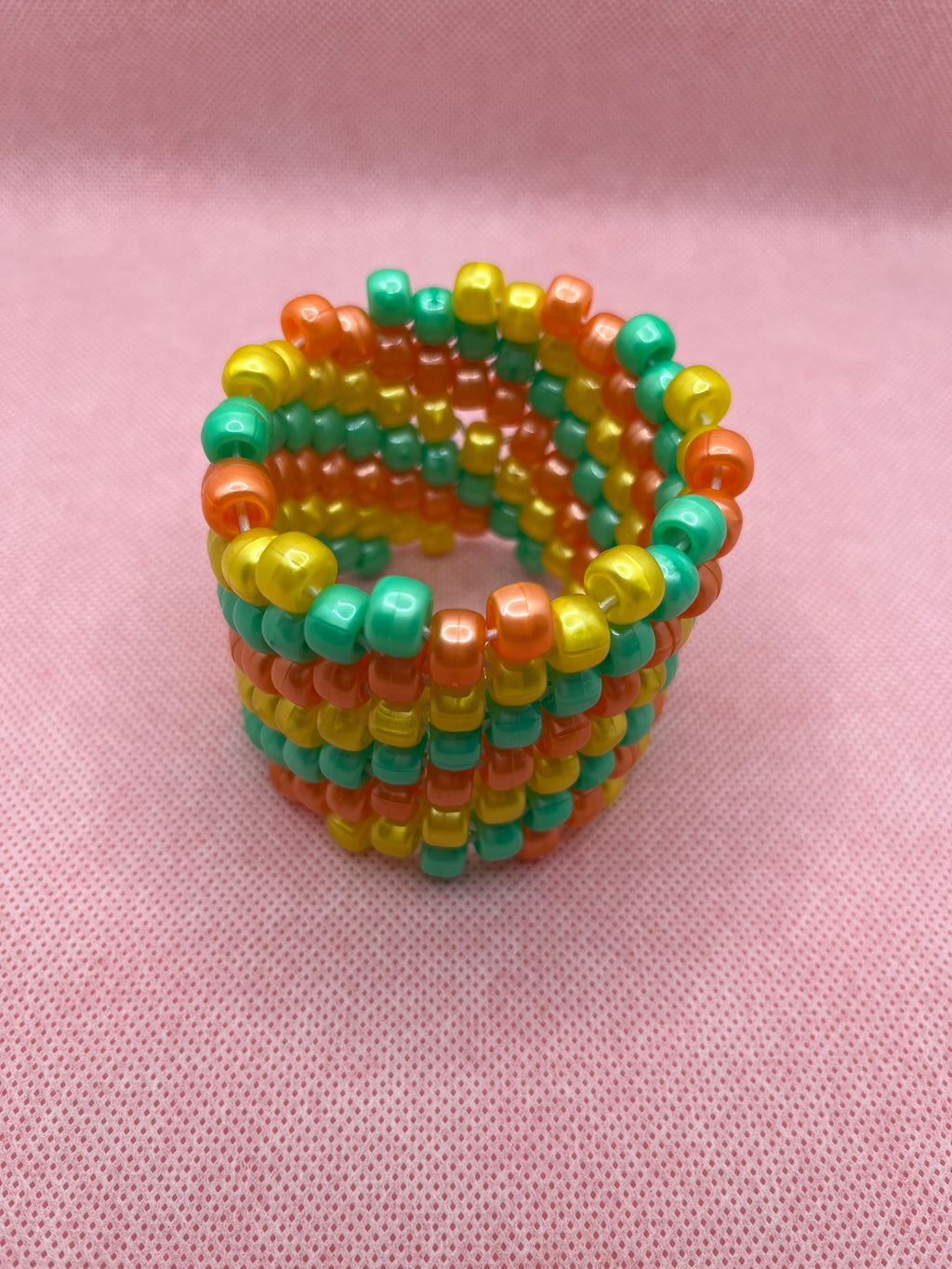 Orange, yellow, and green spiral beaded cuff bracelet against a pink background