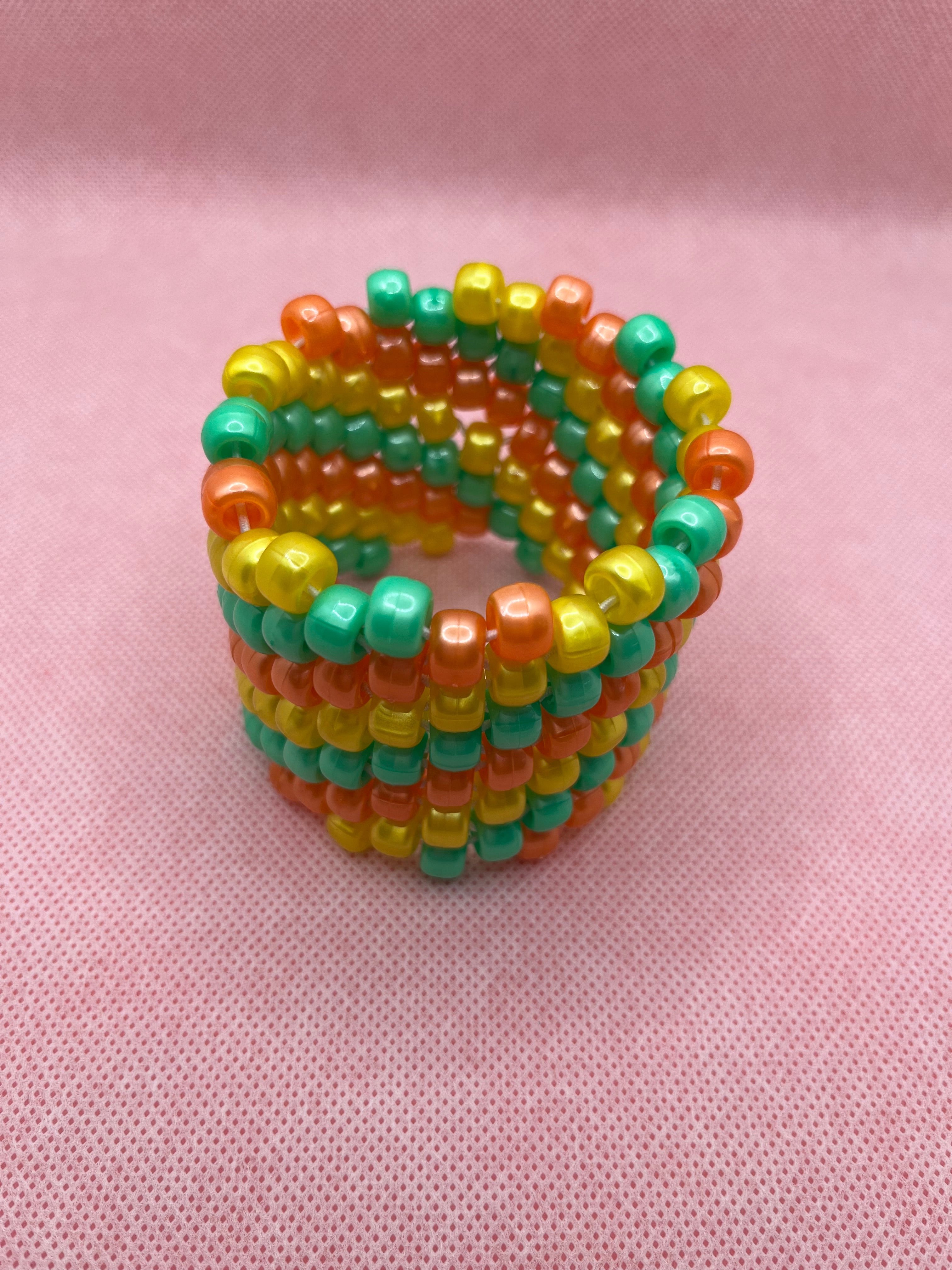 Orange, yellow, and green spiral beaded cuff bracelet against a pink background