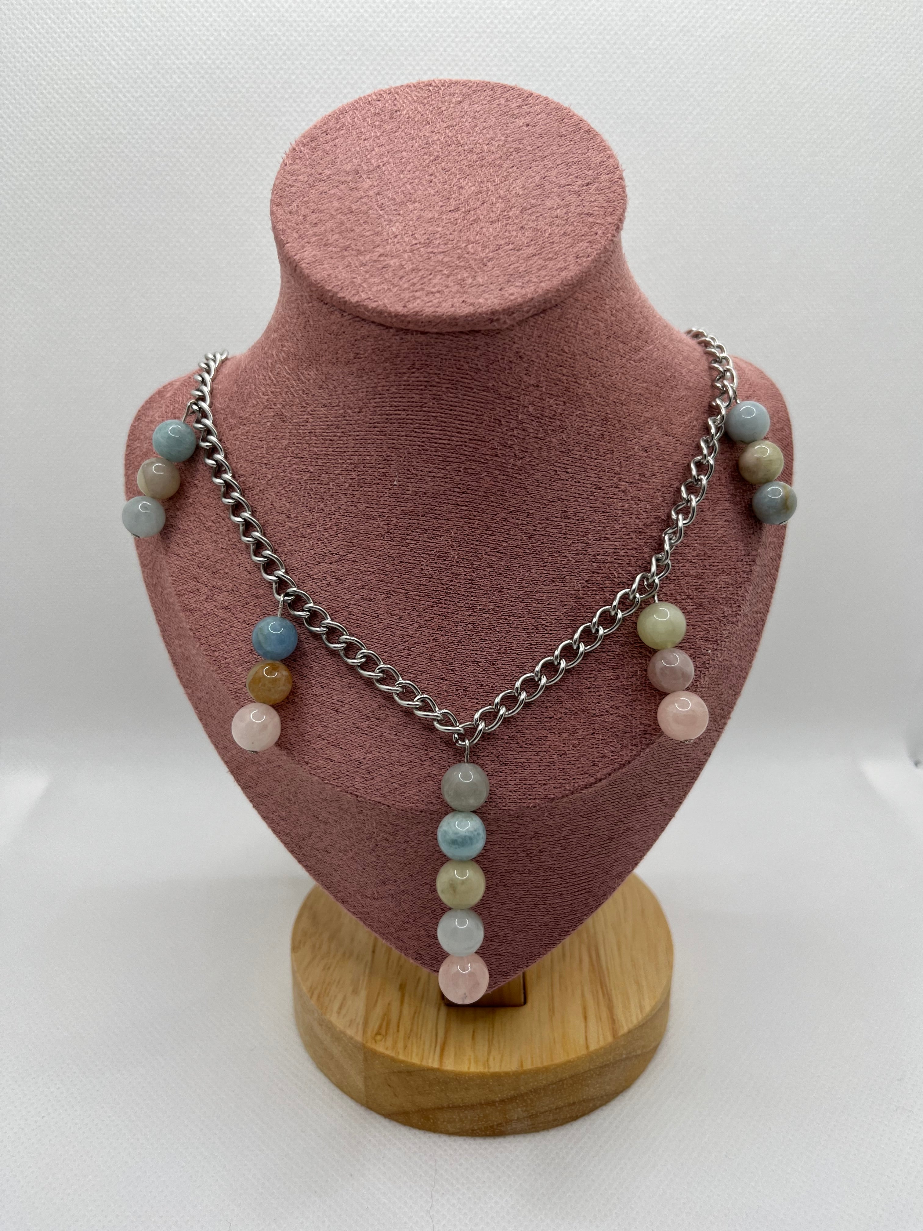 Necklace with multi-bead pastel pendants throughout draped over a blush pink mannequin with a white background.