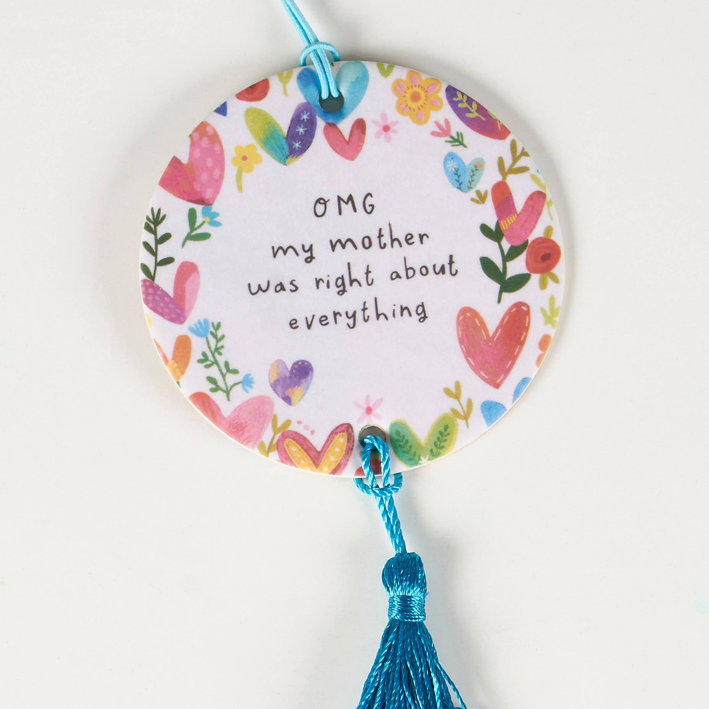 Decorative round car air freshener with colorful hearts and text, tied with a blue string on a white background