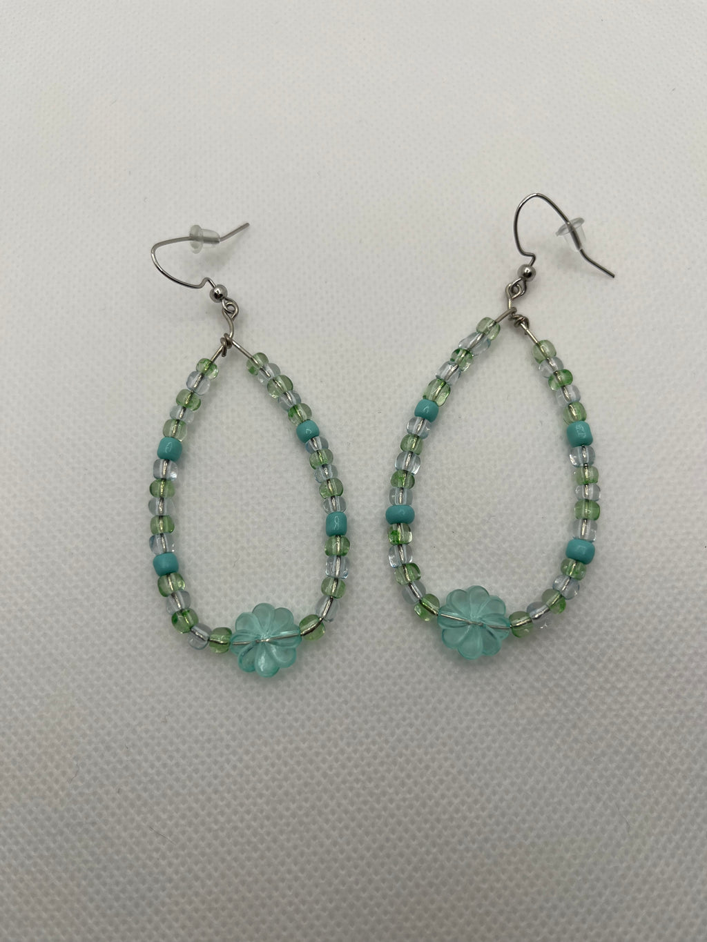 Blue and green beaded earrings with a large transparent clover bead on the bottom against a white background