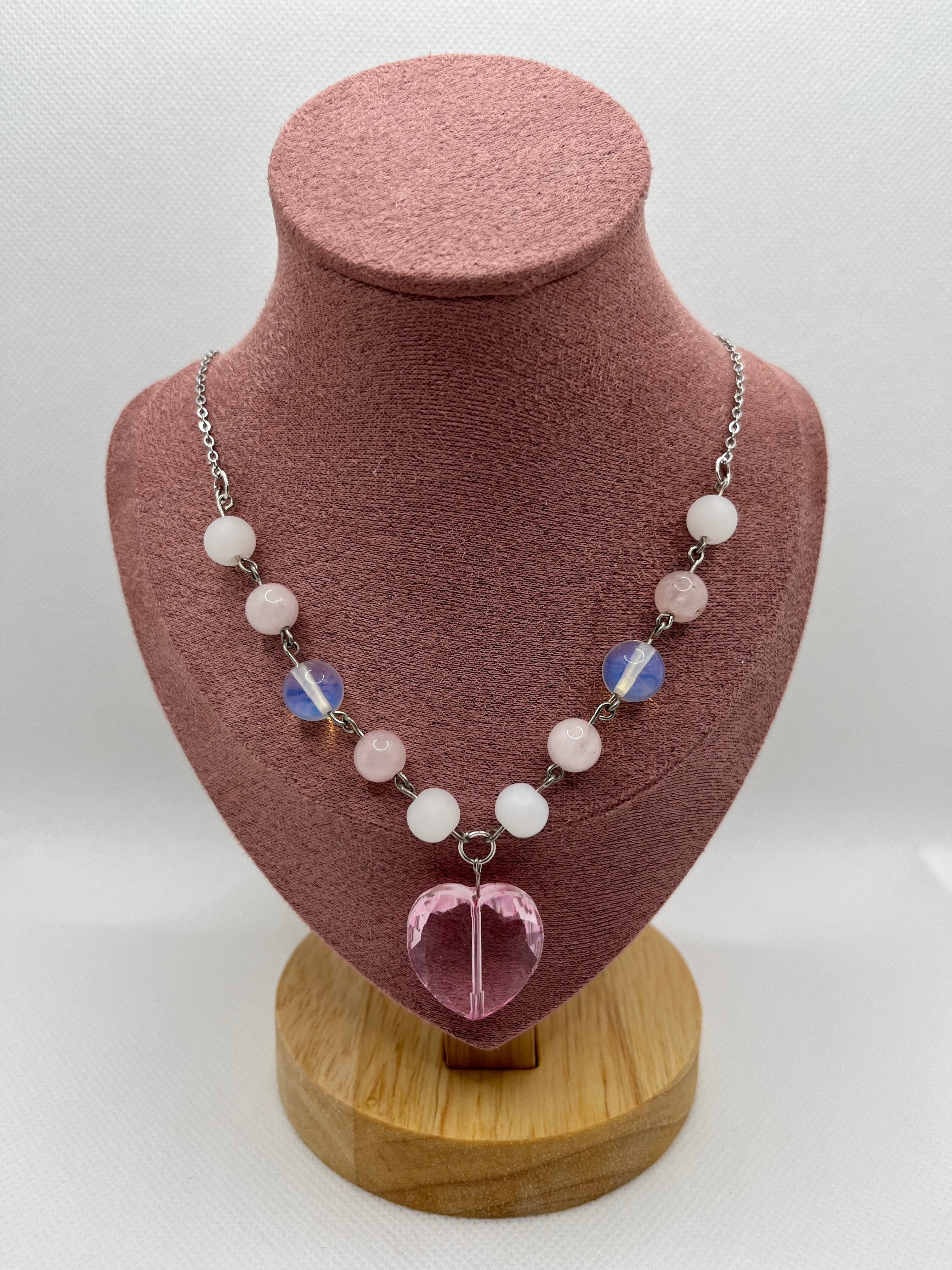 Pink and white necklace with a heart-shaped pendant draped over a blush pink mannequin with a white background.