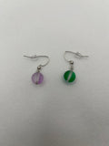 Matte glass earrings with one purple and one green against a white background