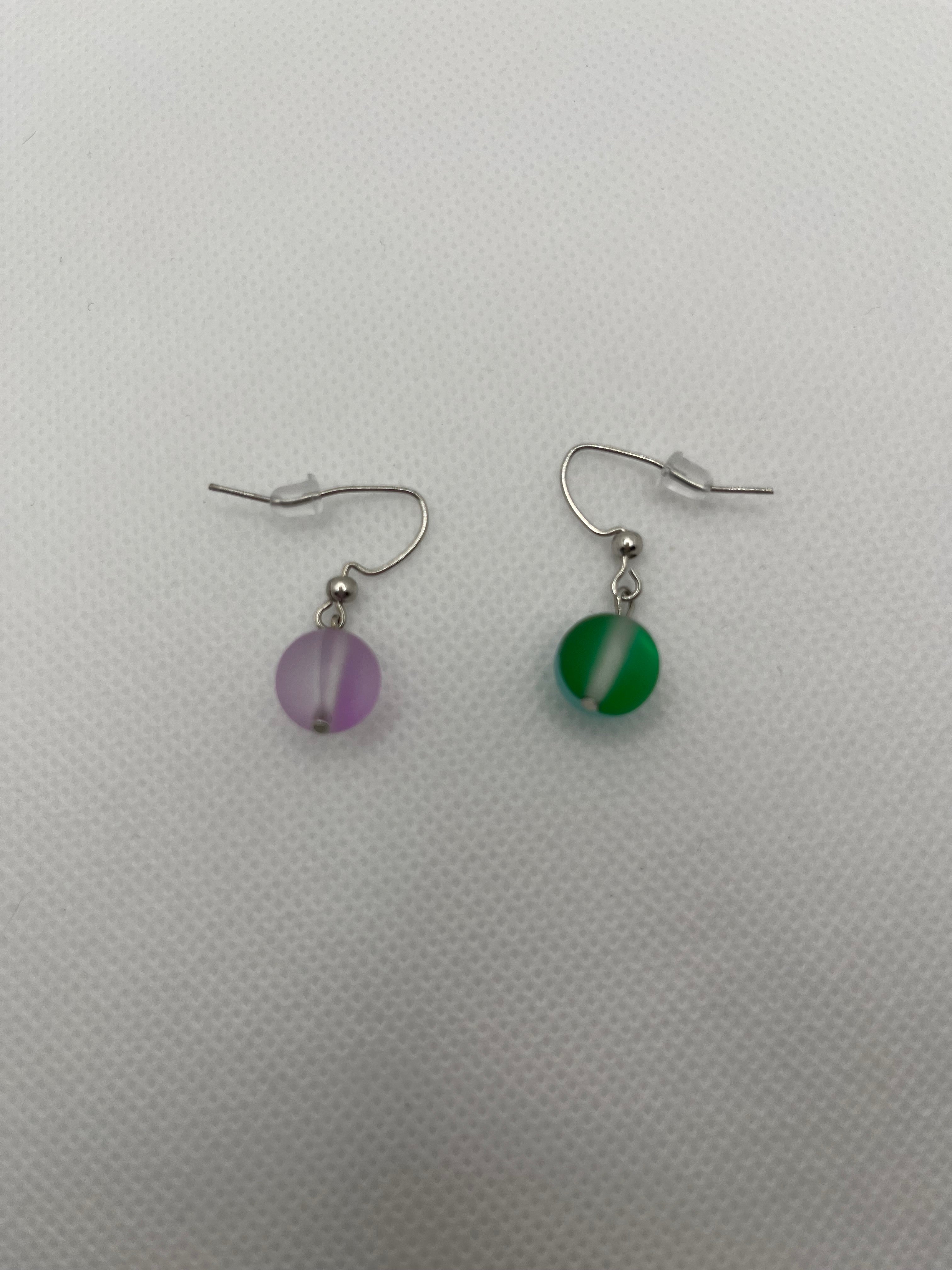 Matte glass earrings with one purple and one green against a white background
