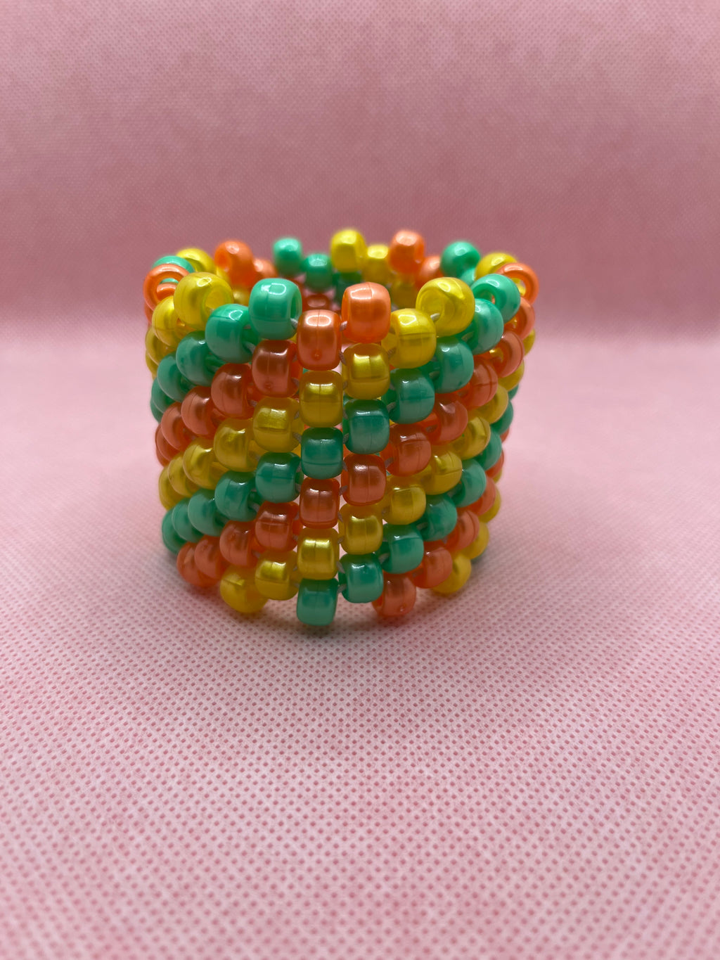 Orange, yellow, and green spiral beaded cuff bracelet against a pink background