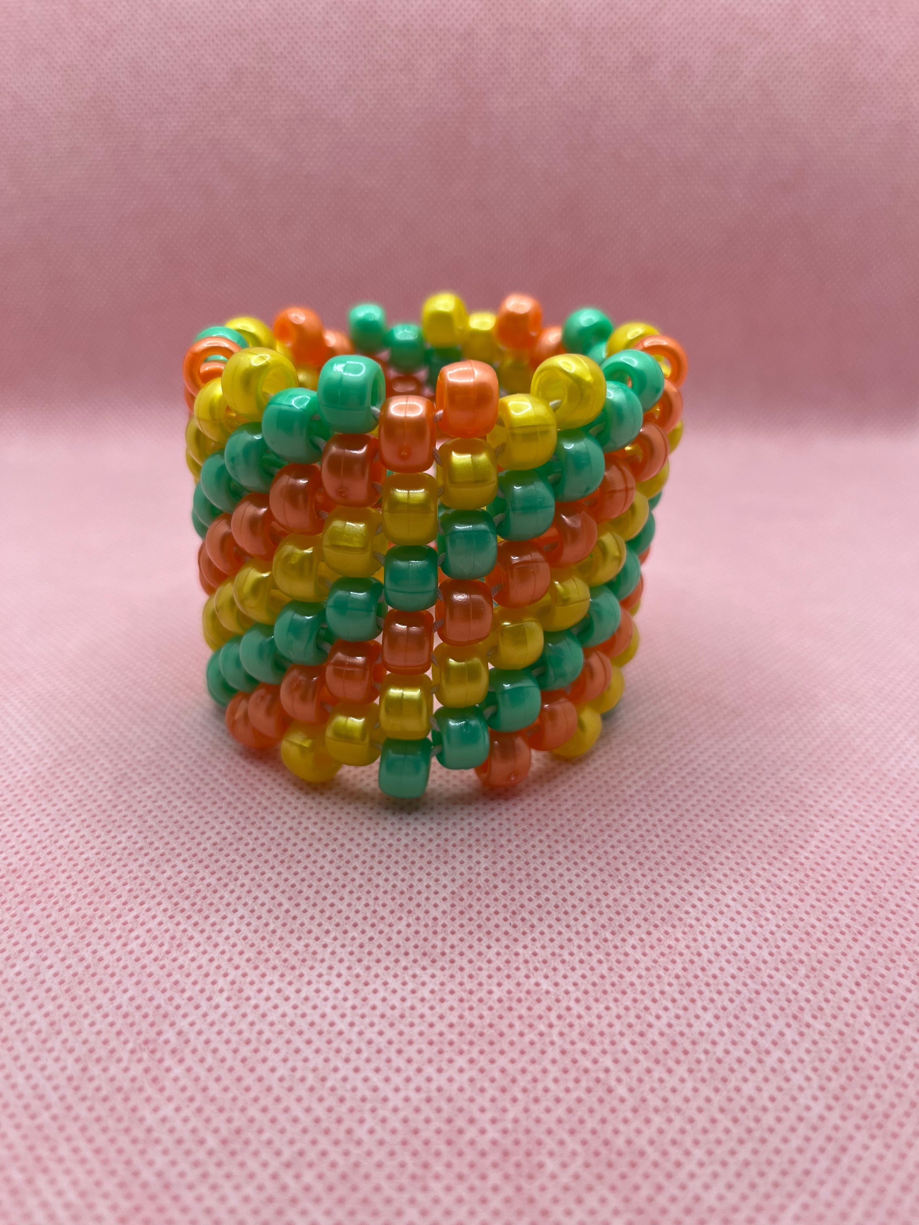 Orange, yellow, and green spiral beaded cuff bracelet against a pink background
