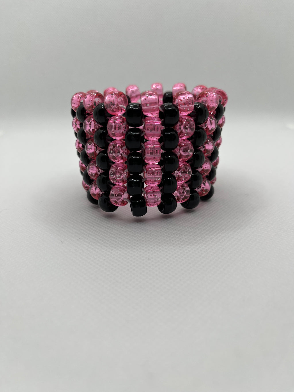Pink glitter and black striped beaded cuff bracelet on a white background.