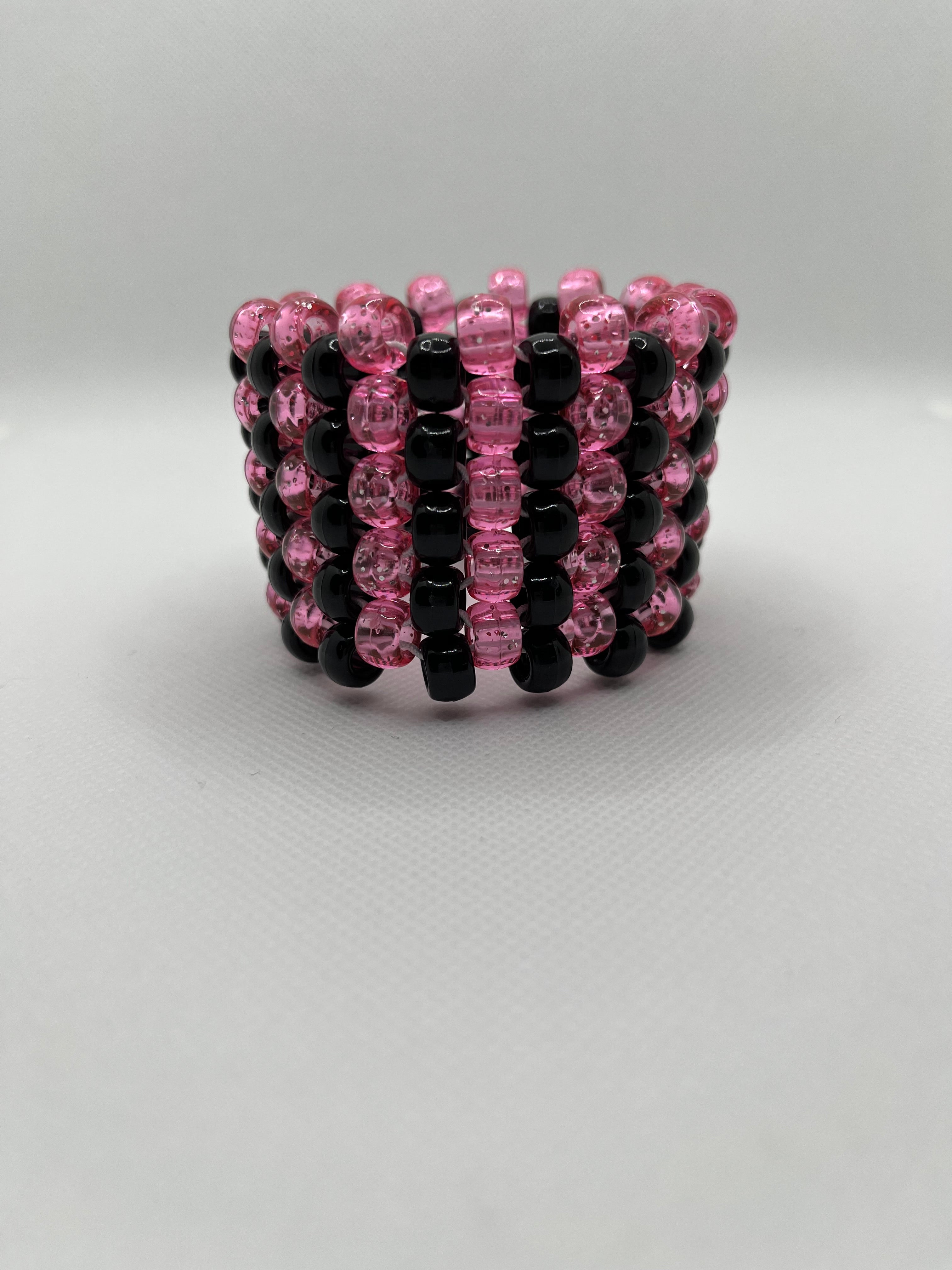 Pink glitter and black striped beaded cuff bracelet on a white background.