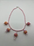 Pink seed bead necklace with silicone beads strung throughout laid flat against a white background.