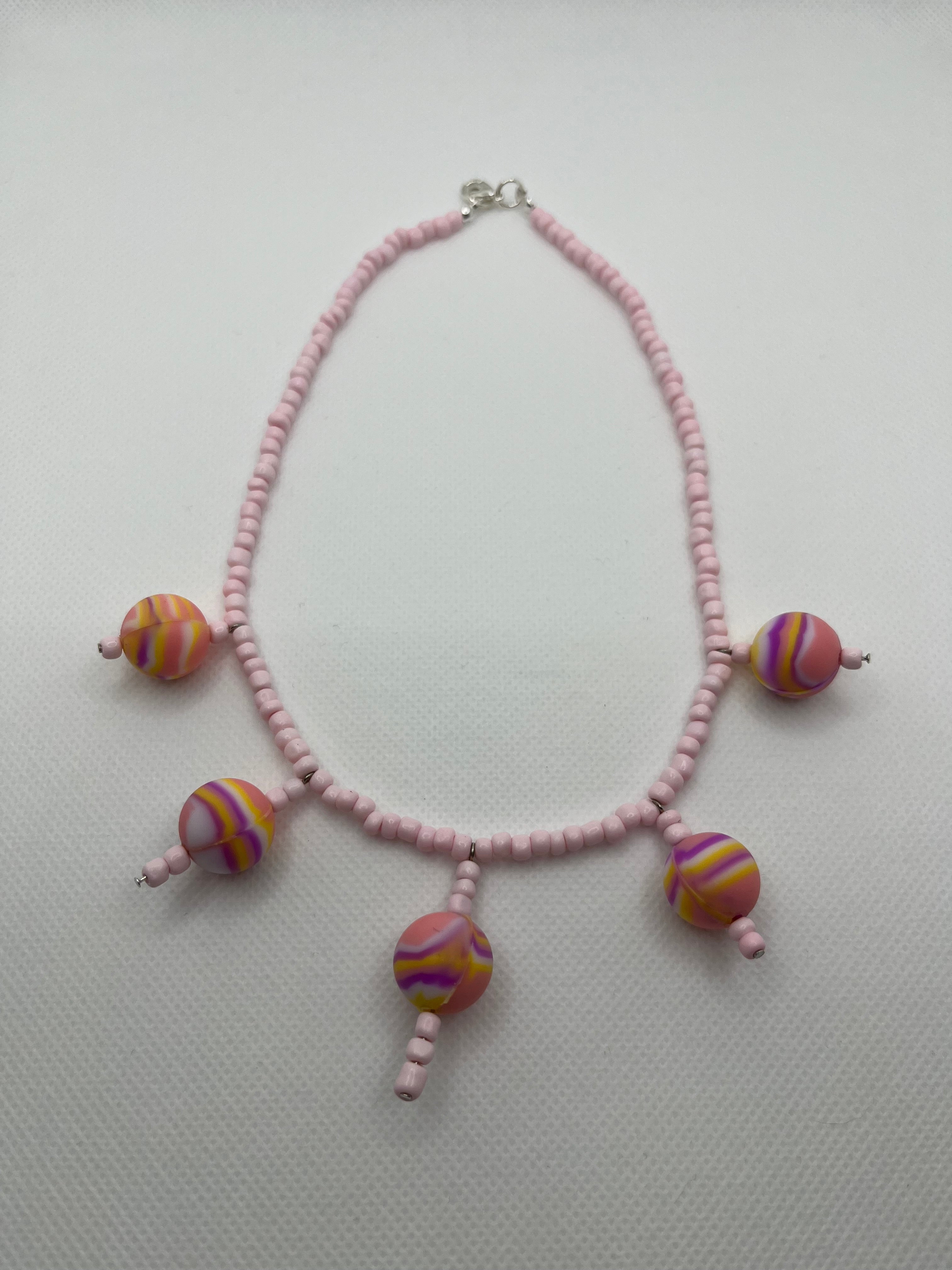 Pink seed bead necklace with silicone beads strung throughout laid flat against a white background.